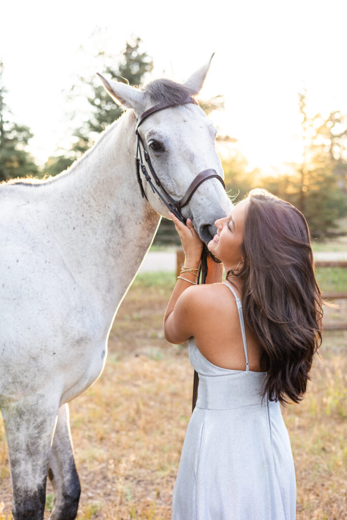 A young woman in a silver dress gets a kiss on the cheek from her white horse.