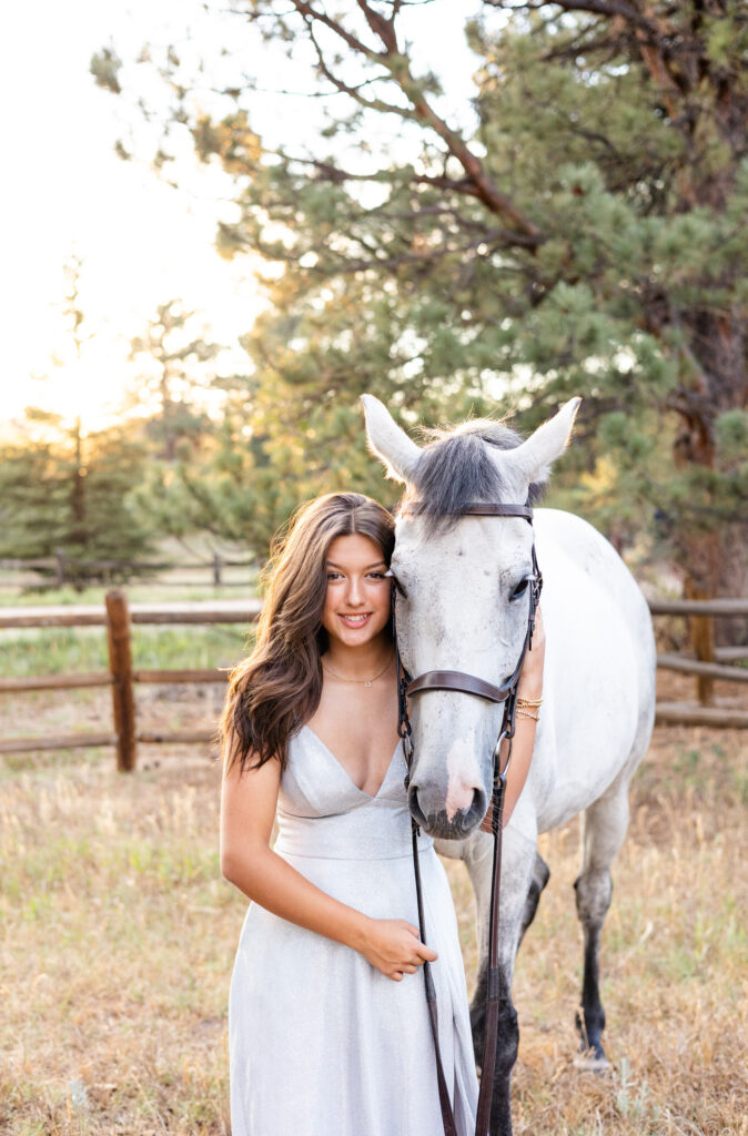 A young woman and her white horse stand side by side as the young woman looks at the camera.