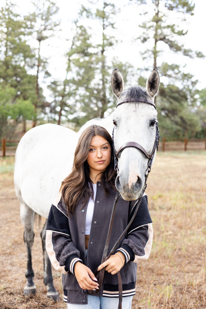 A young woman looks at the camera as her horse stands over her shoulder also looking at the camera.