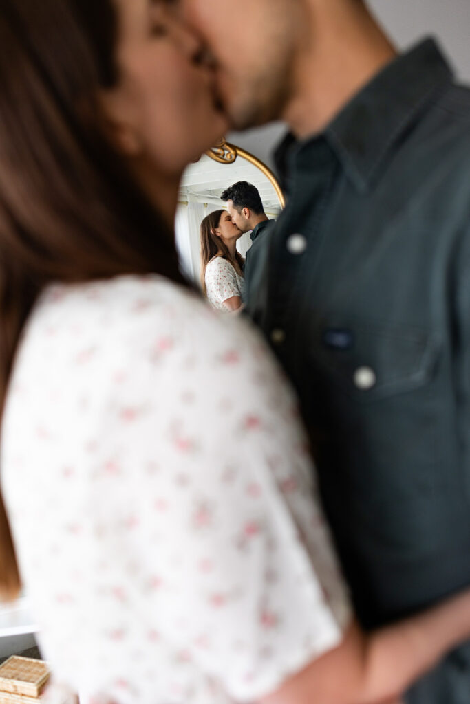 A couple shares a kiss in front of a mirror.