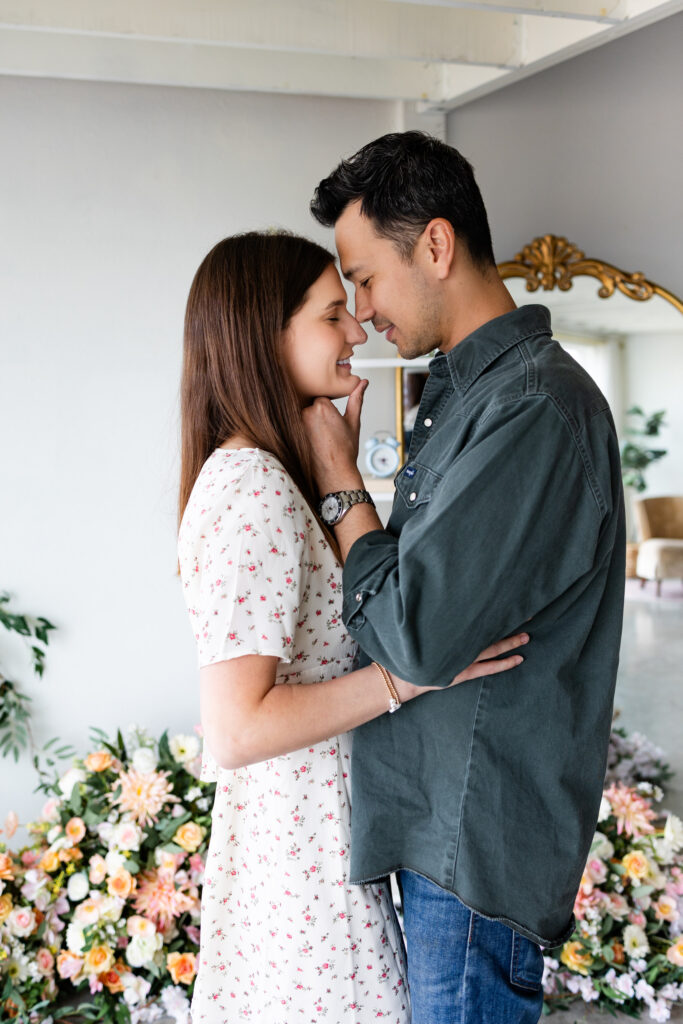 Husband and wife stand forehead to forehead in a studio filled with flowers.