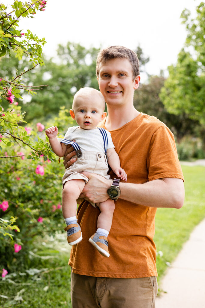 A dad holds his baby boy and they both look at the camera. 