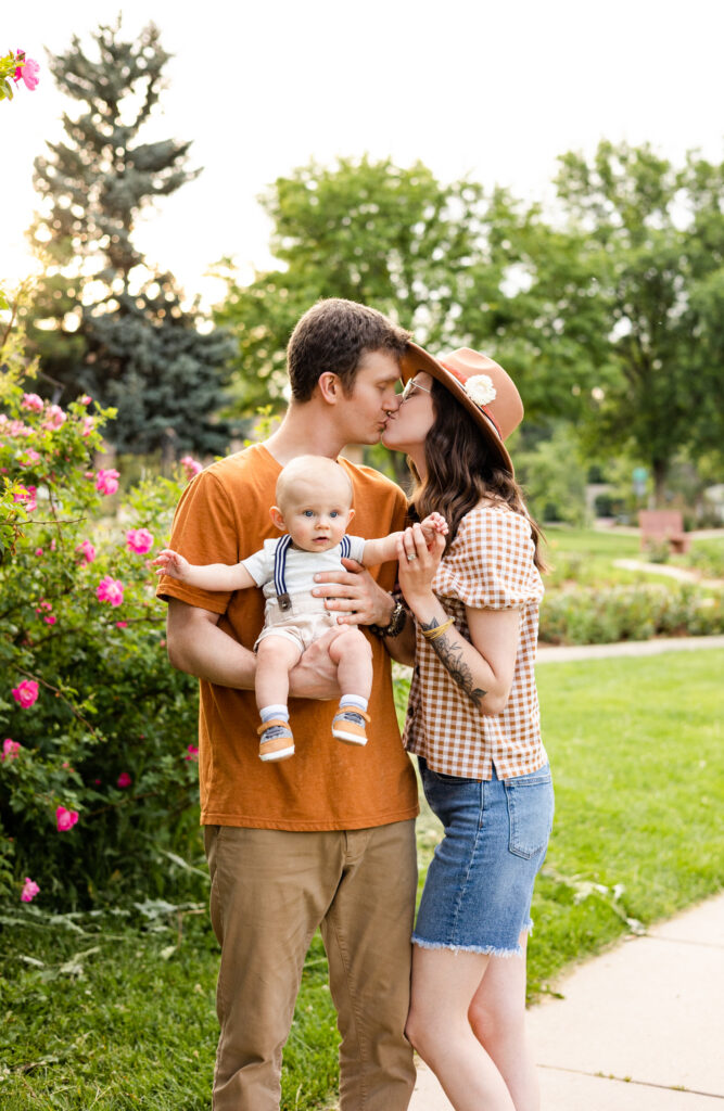 A mom and dad share a kiss as they hold their baby boy between them.