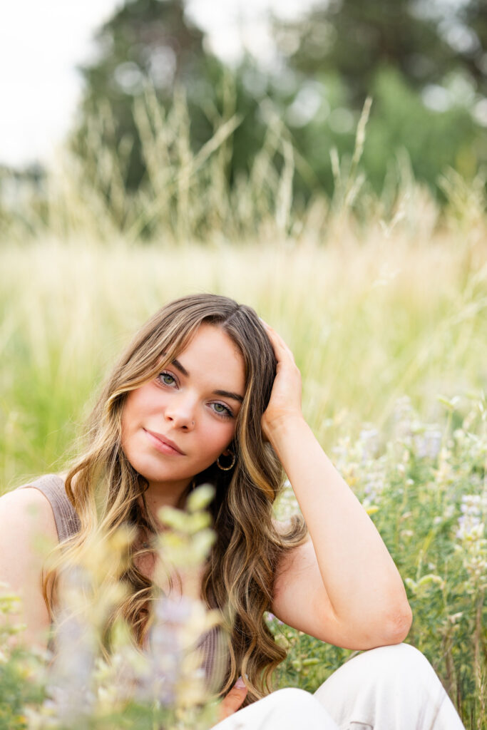 A young woman sits in a field of wildflowers and smiles at the camera.