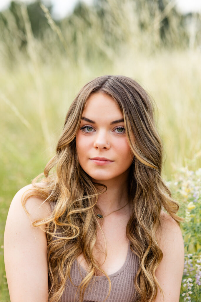 A young woman sits in a field with tall grass and smiles at the camera.