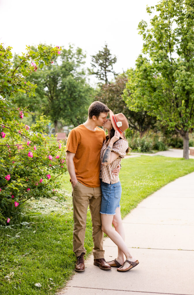 A couple shares a kiss in a rose garden.