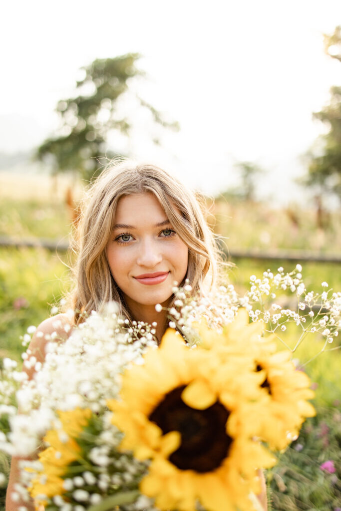 A woman smiles at the camera over a bouquet of sunflowers and baby's breath.