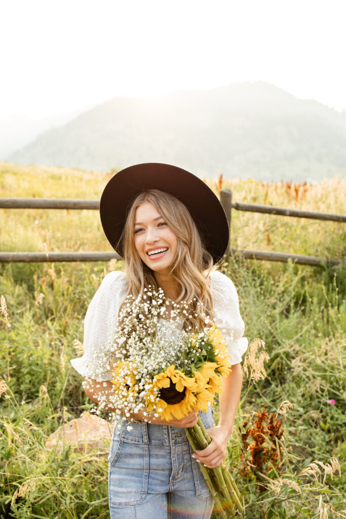 A young woman smiles at the camera holding a bouquet of sunflowers and baby's breath.