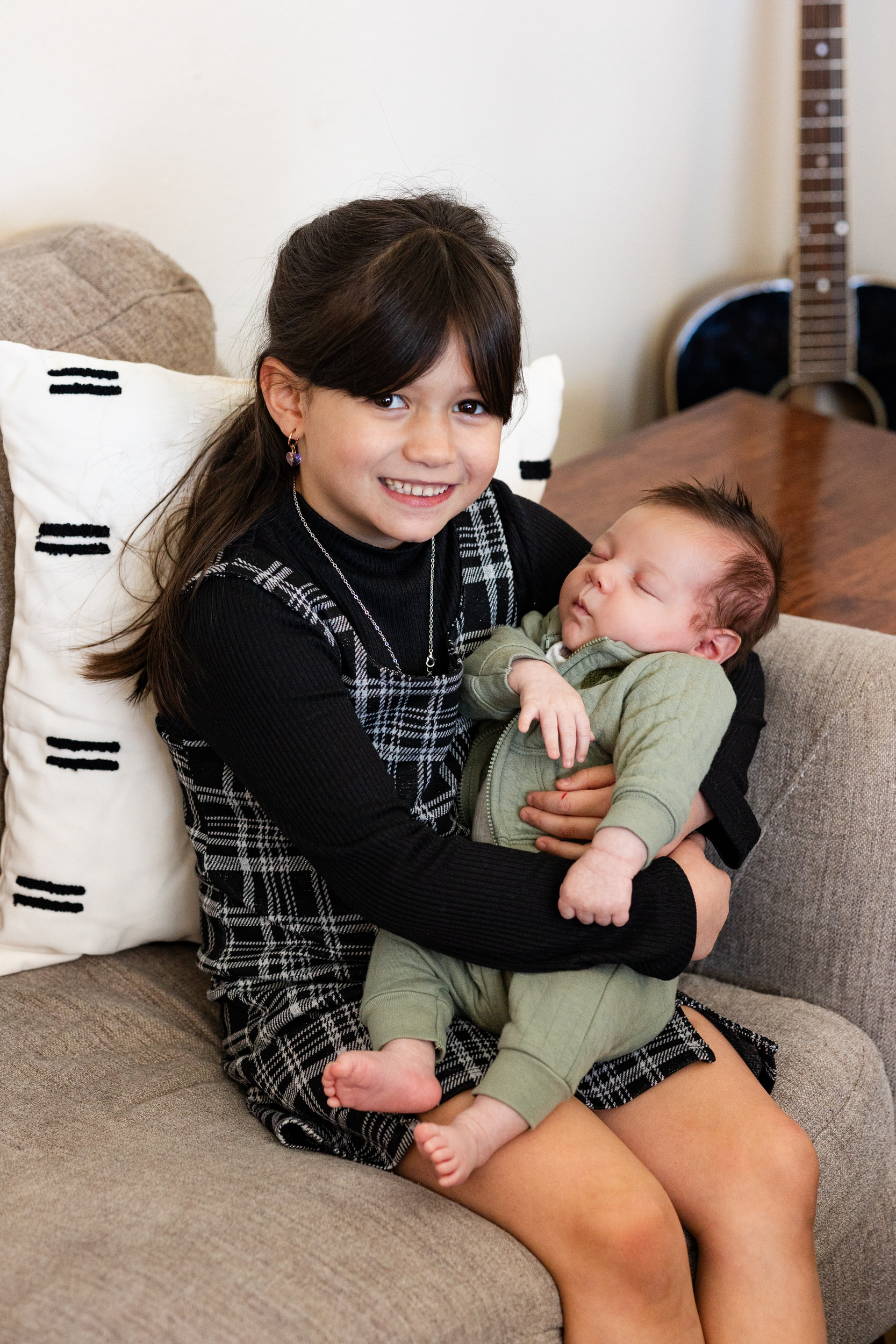 Older sister holds newborn baby brother and smiles.