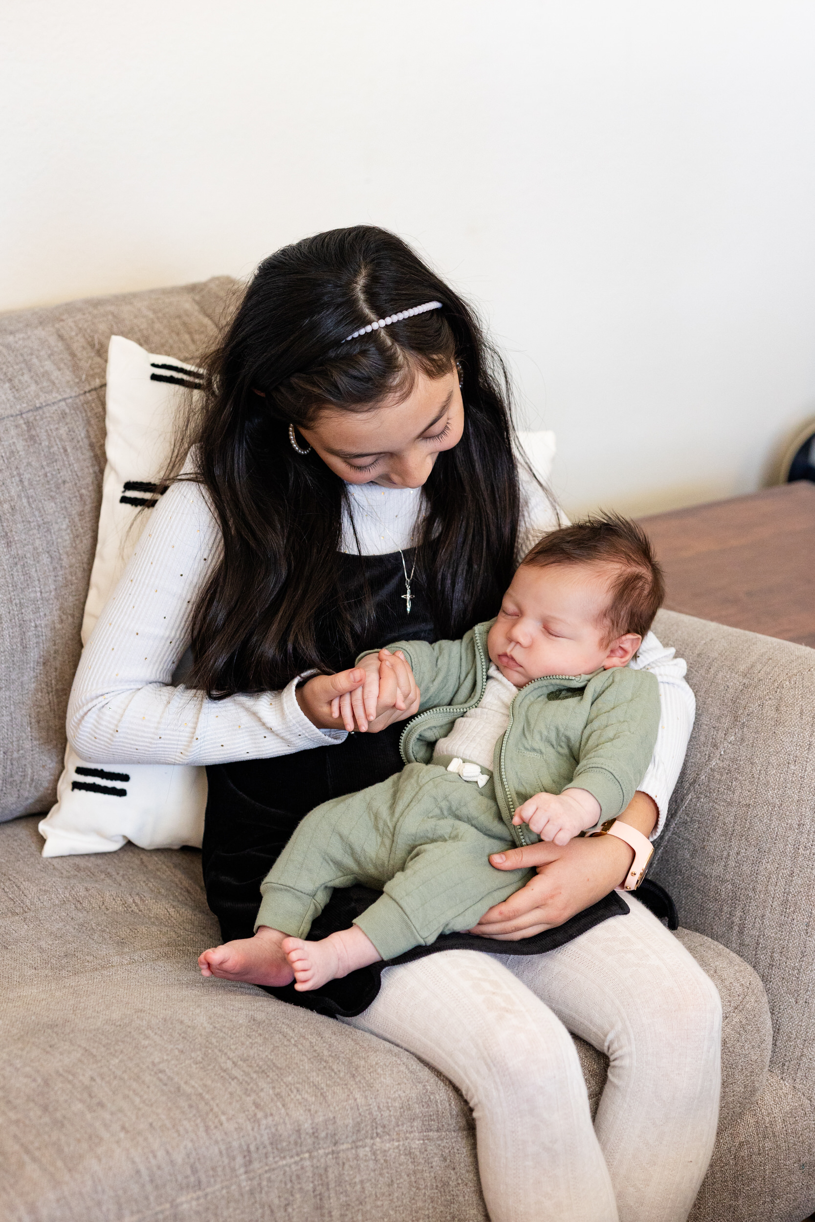 Older sister holds and smiles at newborn baby brother.