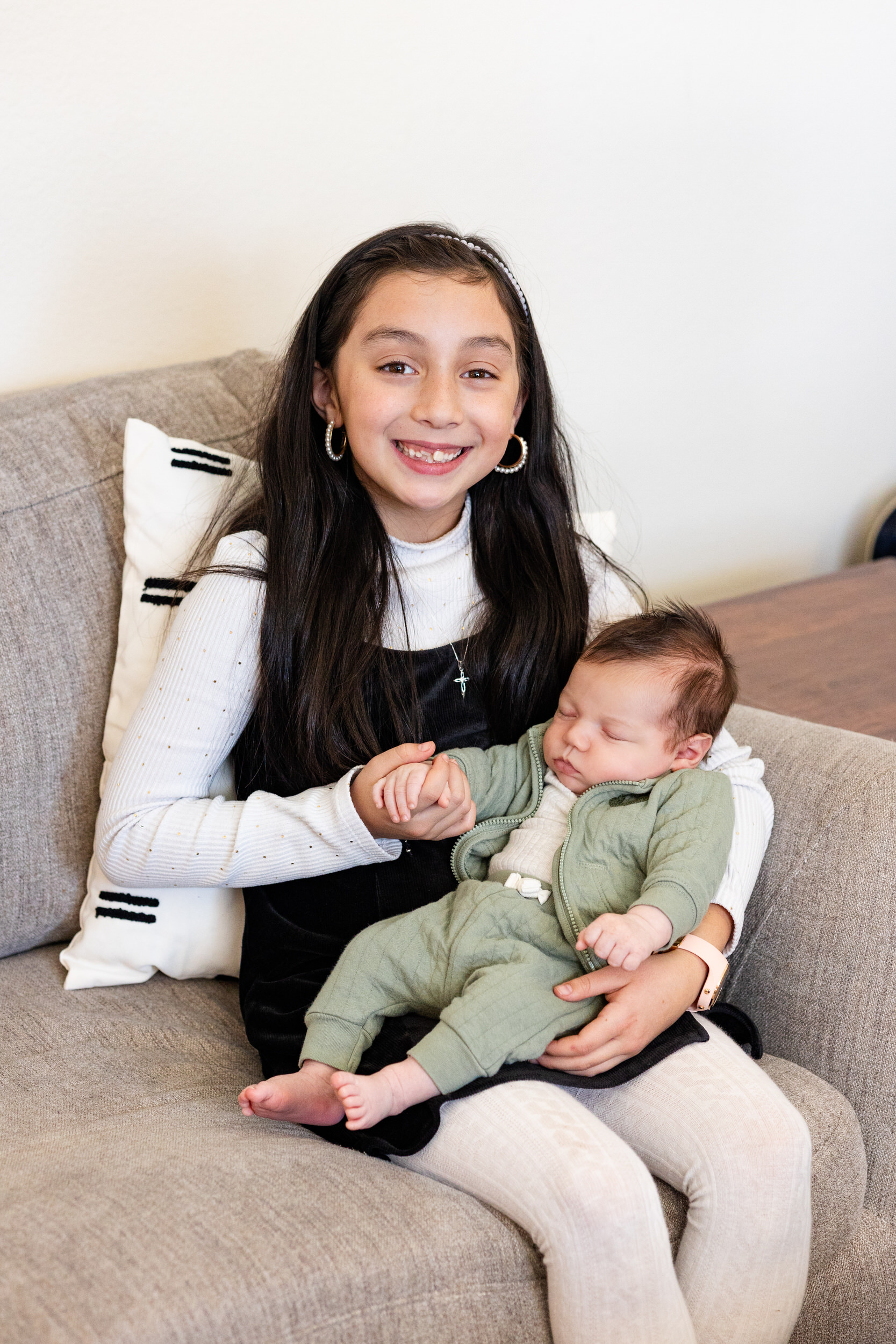Older sister holds newborn baby brother and smiles at the camera.