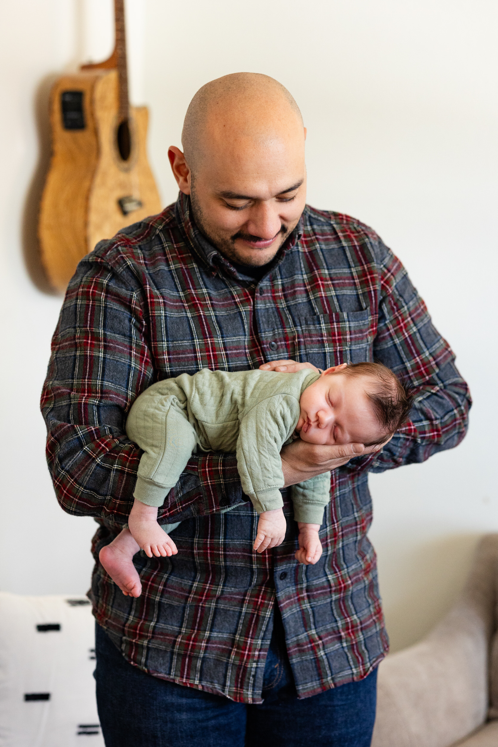 Dad holds sleeping newborn baby in his arms and smiles down at him.
