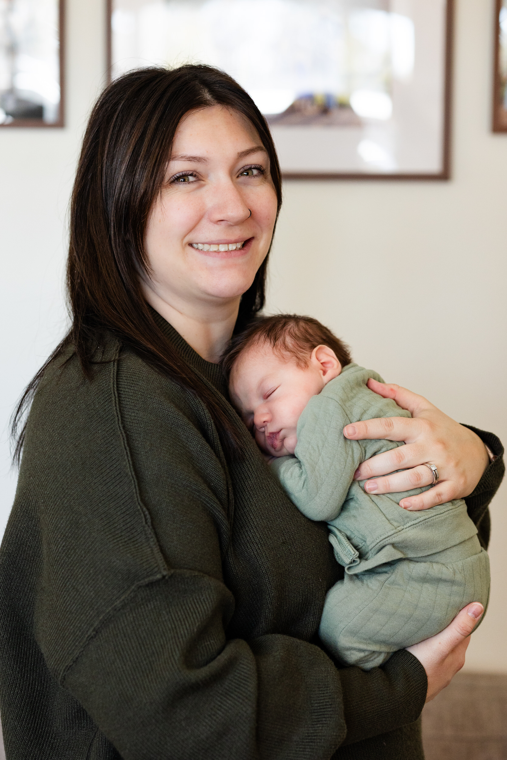 Newborn baby sleeps on his mom's chest and she smiles at the camera.