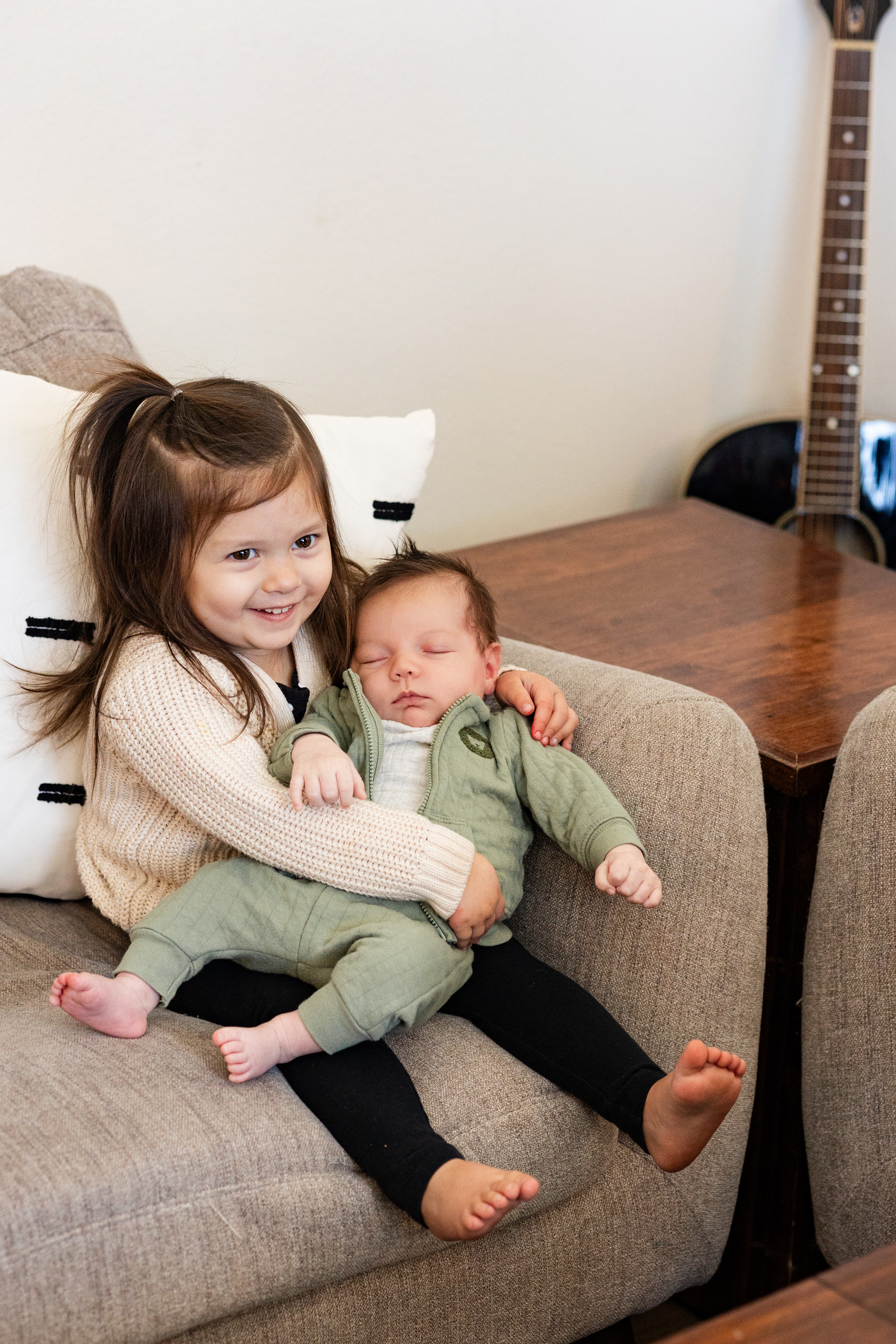 Older sister holds newborn baby brother and smiles.