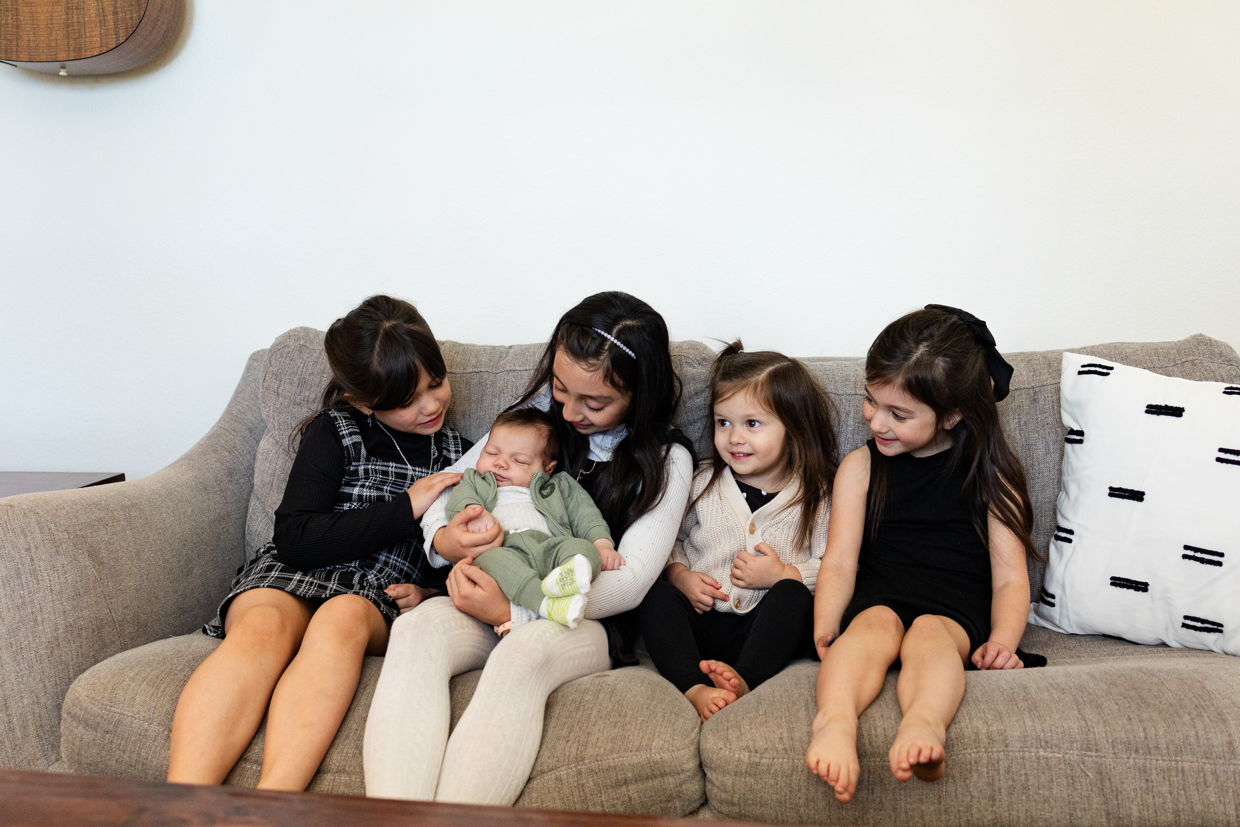 Four young sisters hold and smile at their newborn baby brother.