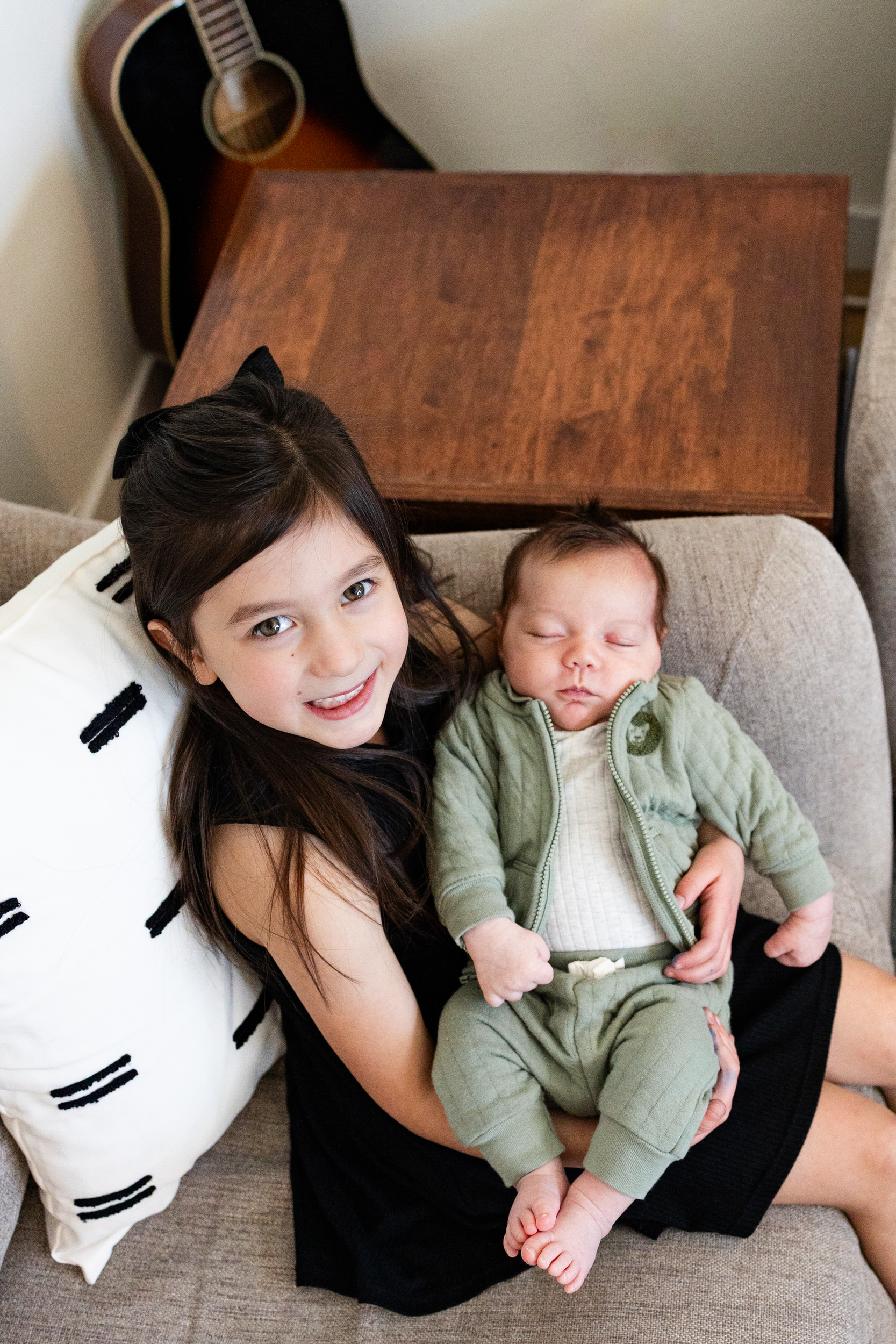 An older sister holds her newborn baby brother and smiles.