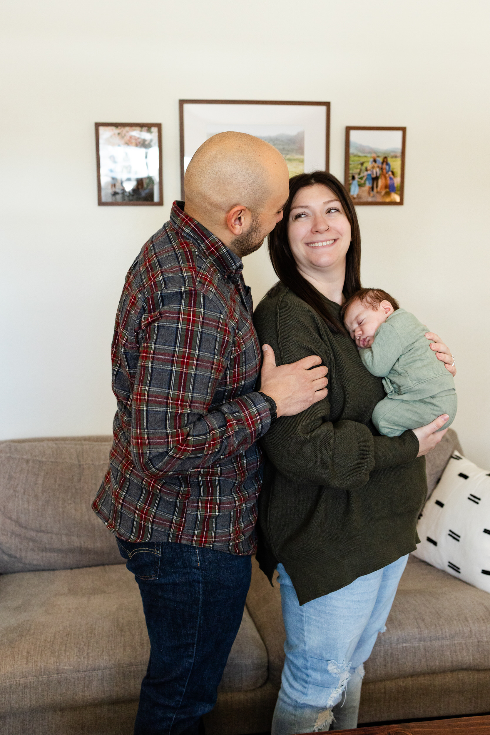 Mom and dad look at each other and smile while mom holds sleeping newborn baby boy against her chest.