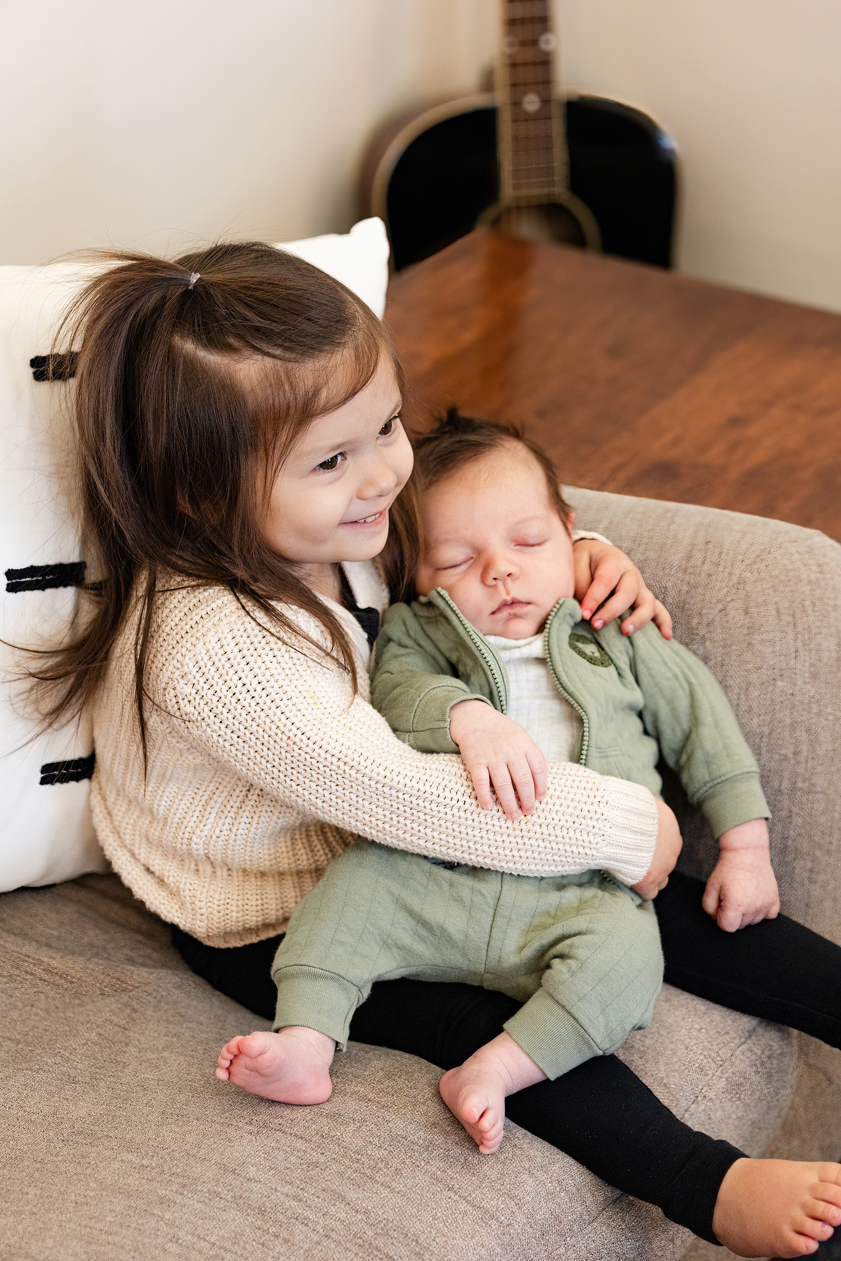Older sister holds newborn baby brother and smiles.