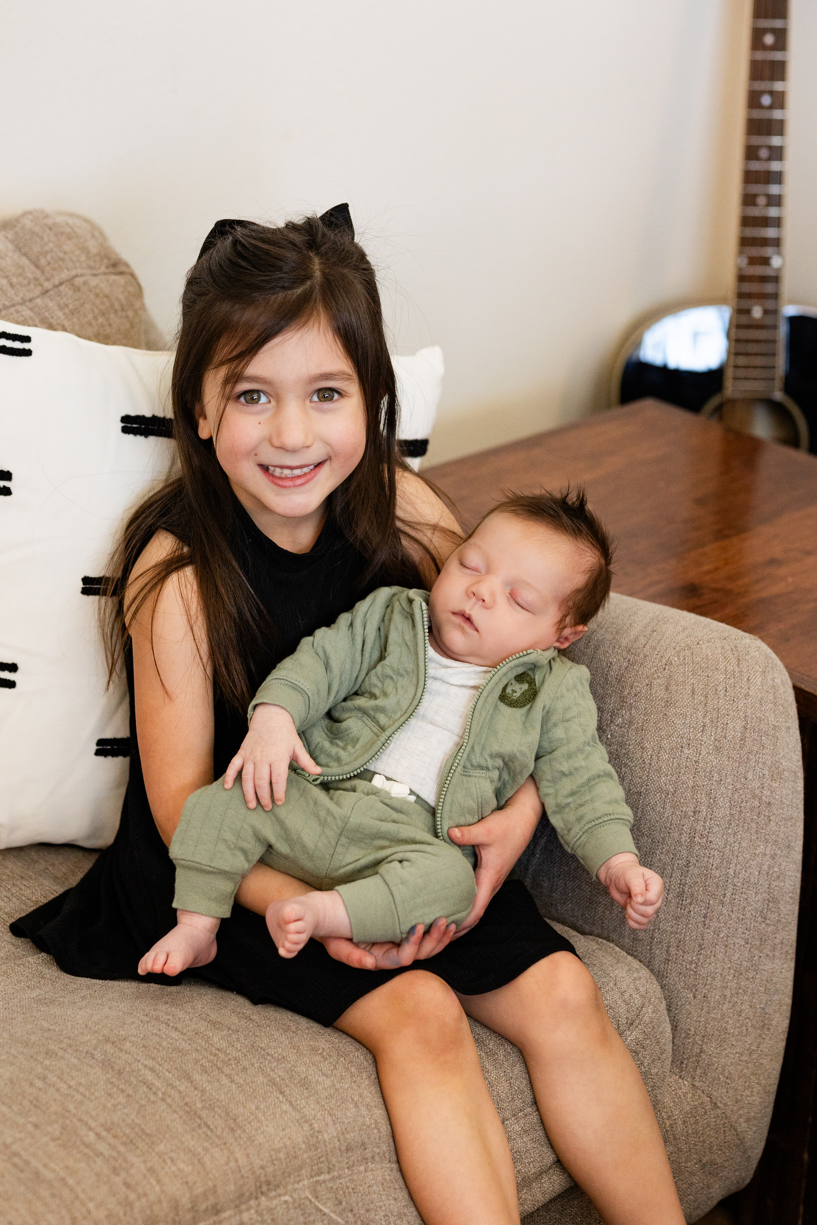 Older sister holds newborn baby brother and smiles at the camera.