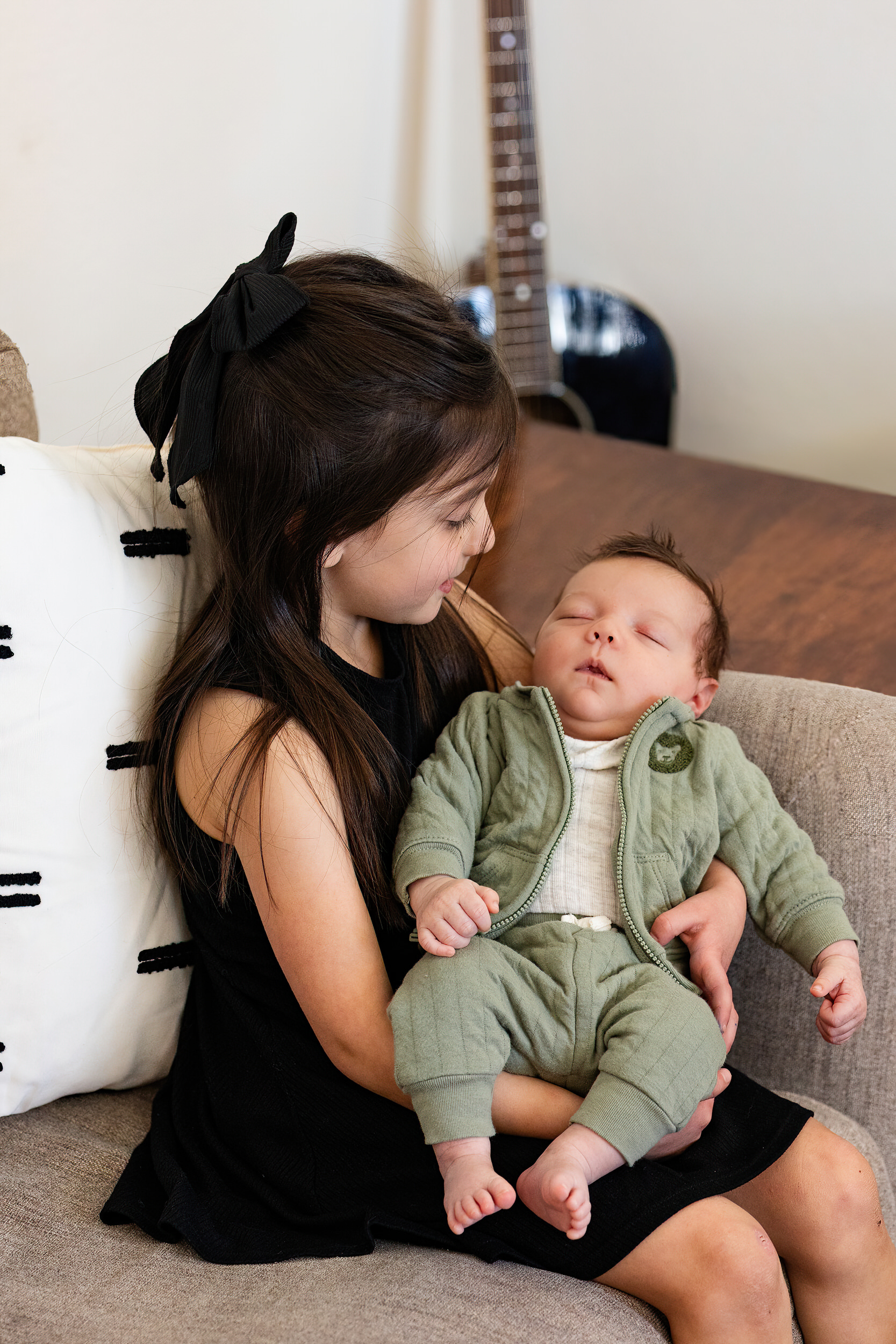 Older sister holds and smiles at newborn baby brother.