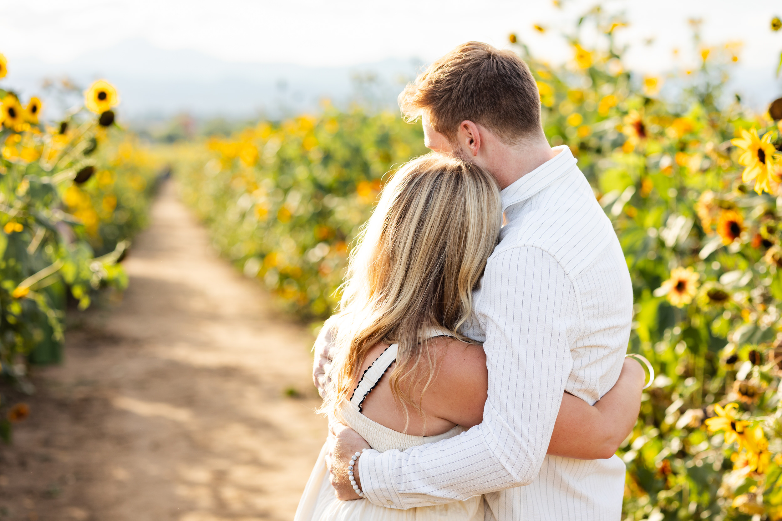 An engaged couple hugs in a sunflower field shortly after the proposal.