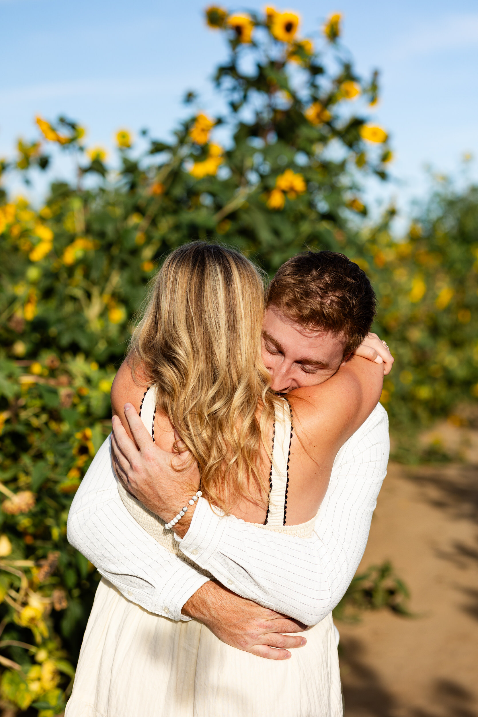 A newly engaged couple hugs in a sunflower field right after the proposal.