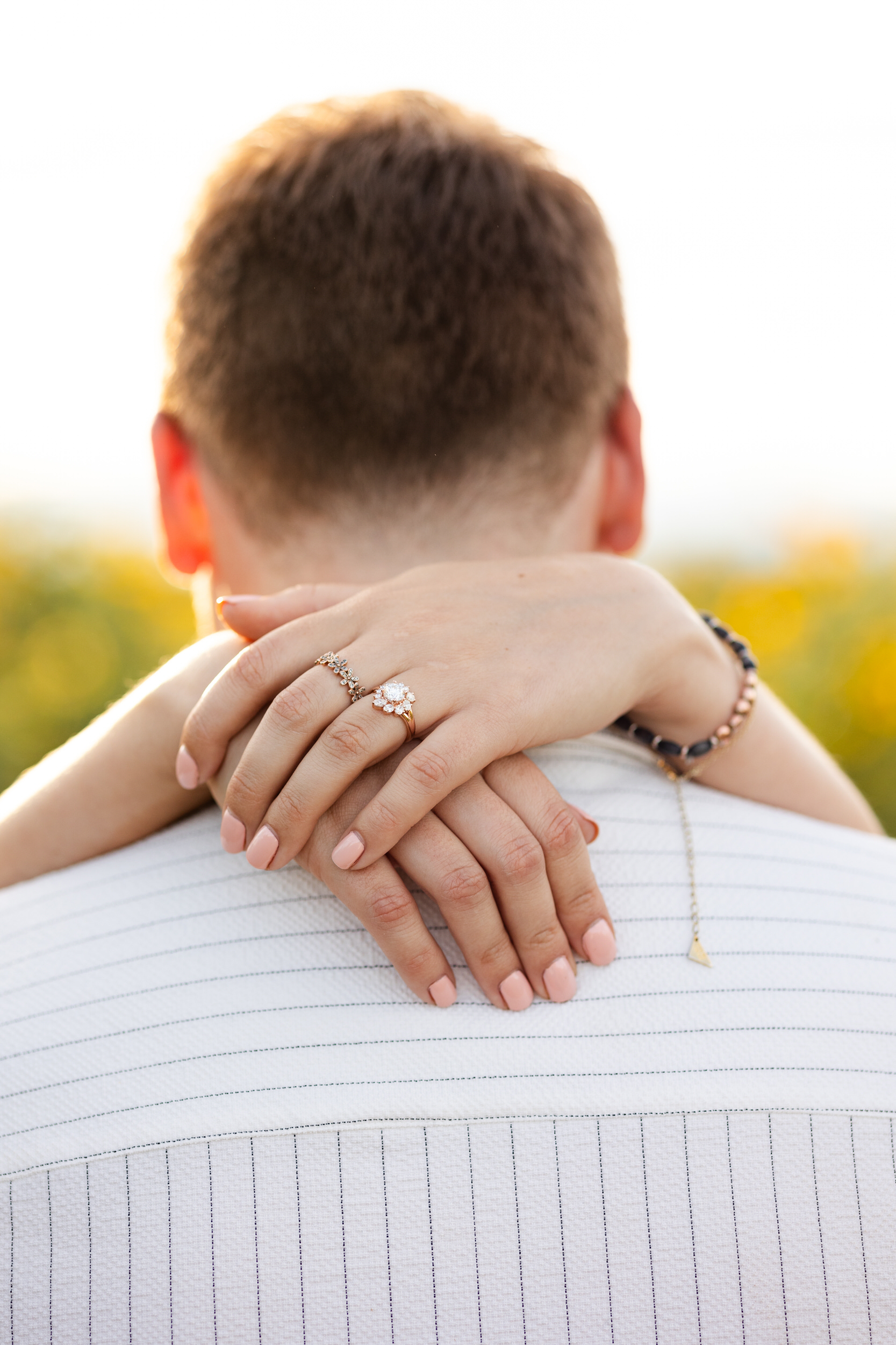 Close up of an engagement ring on a woman's hand as she hugs her fiancé around his neck.