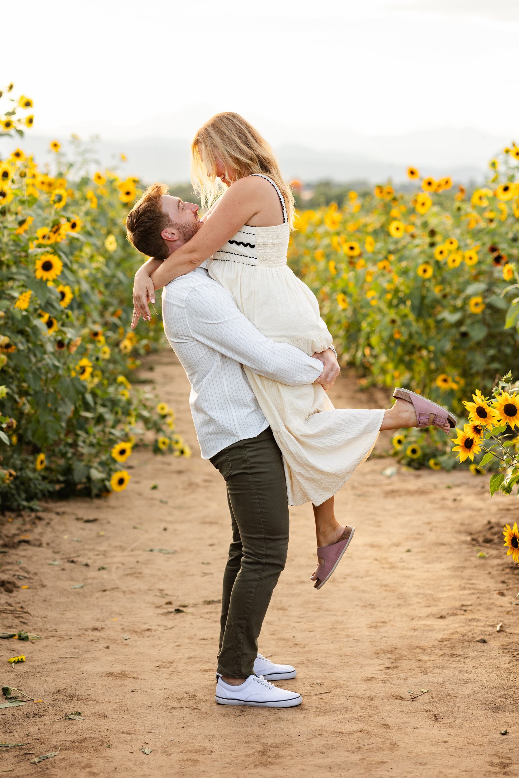A man lifts his fiancée in a sunflower field.