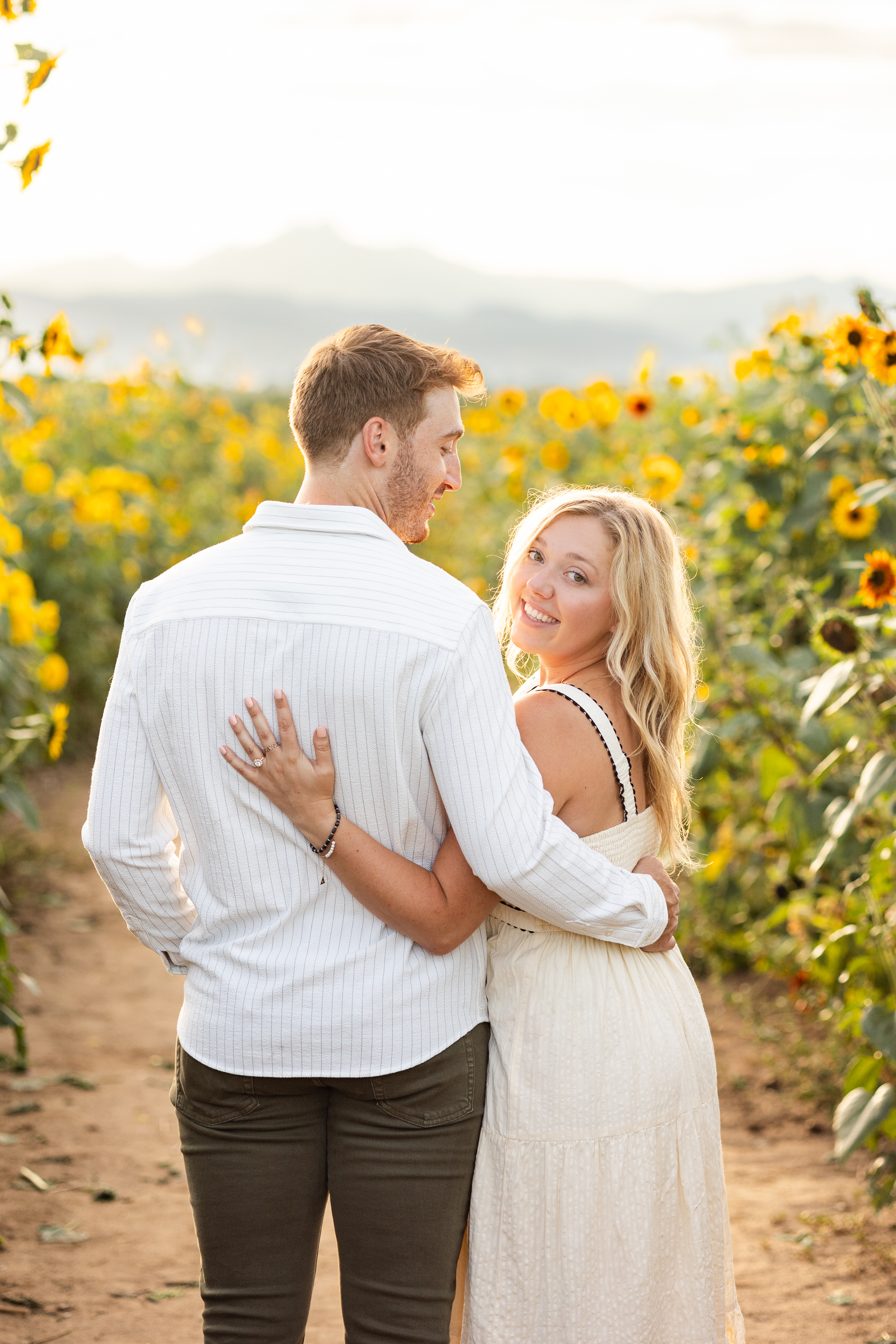 A man has his arm around his fiancée's waist as she looks back over her shoulder and smiles at the camera.