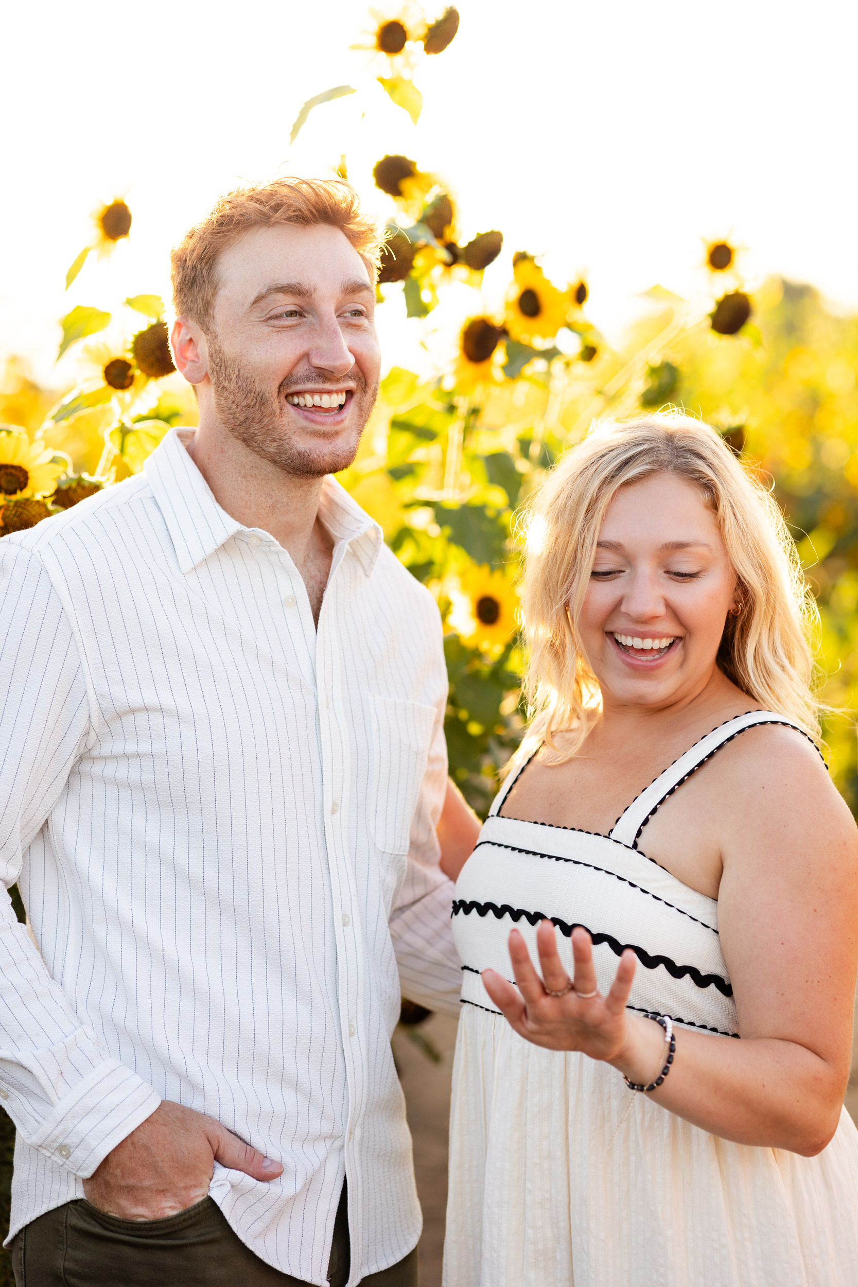 A woman looks at her new engagement ring and smiles while her fiancé is laughing.