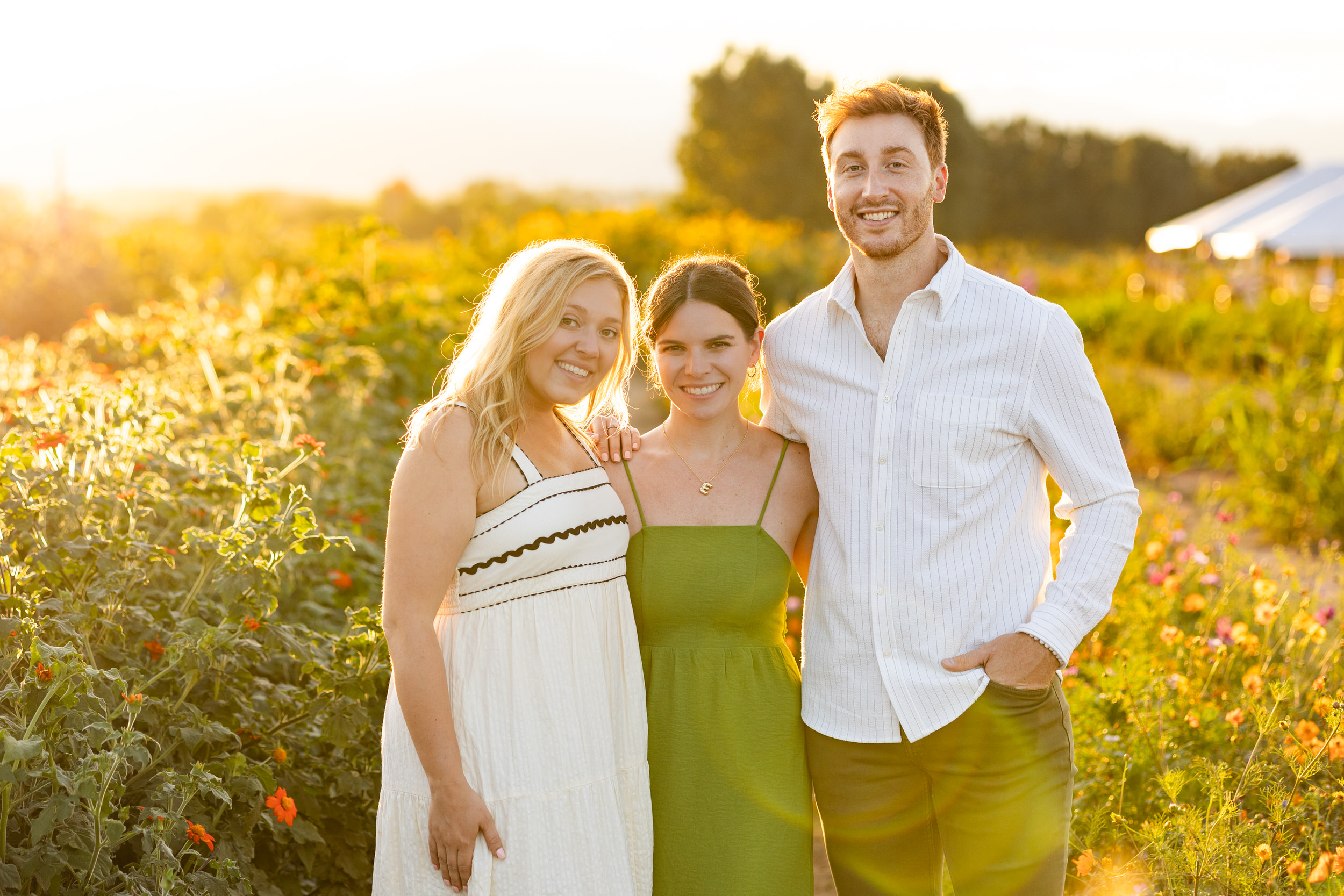 A newly engaged couple smiles at the camera with the friend who helped with the proposal.