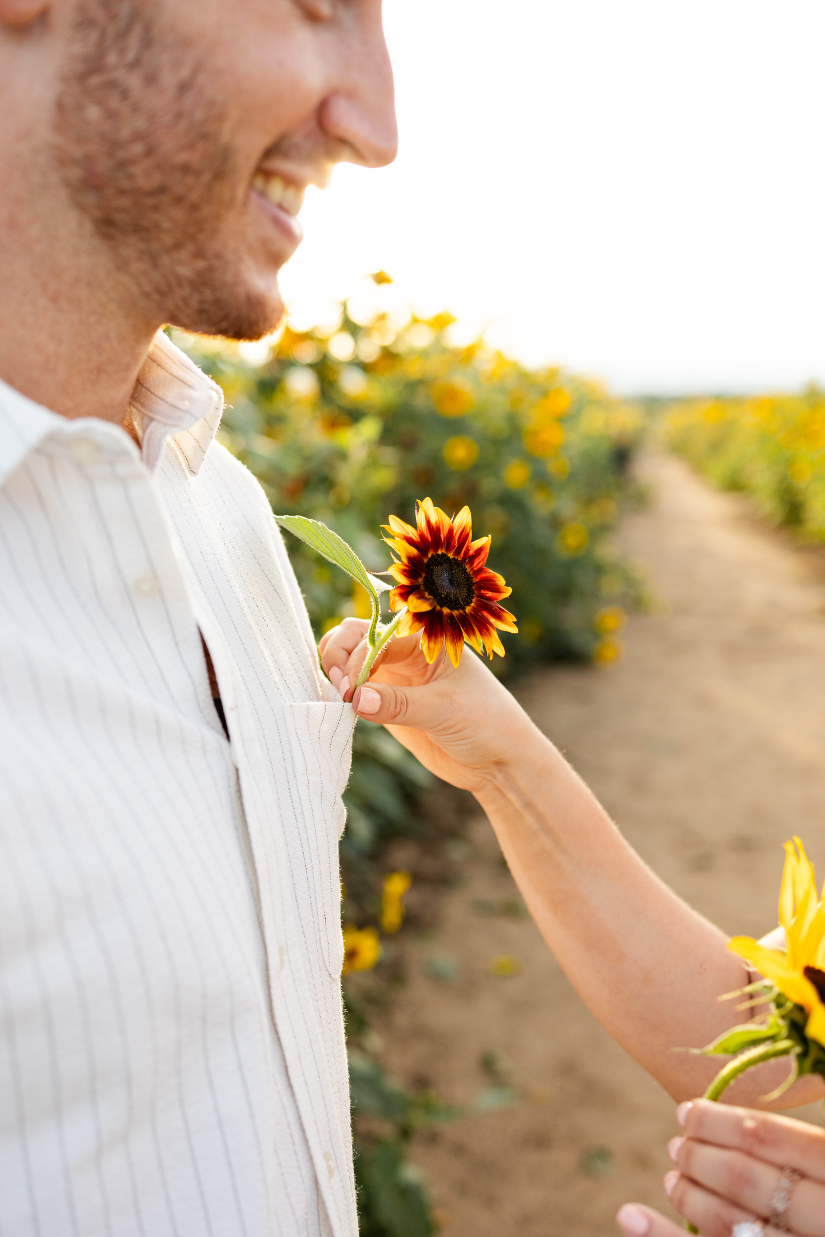 A woman is placing a sunflower in the pocket of her fiancé's shirt.