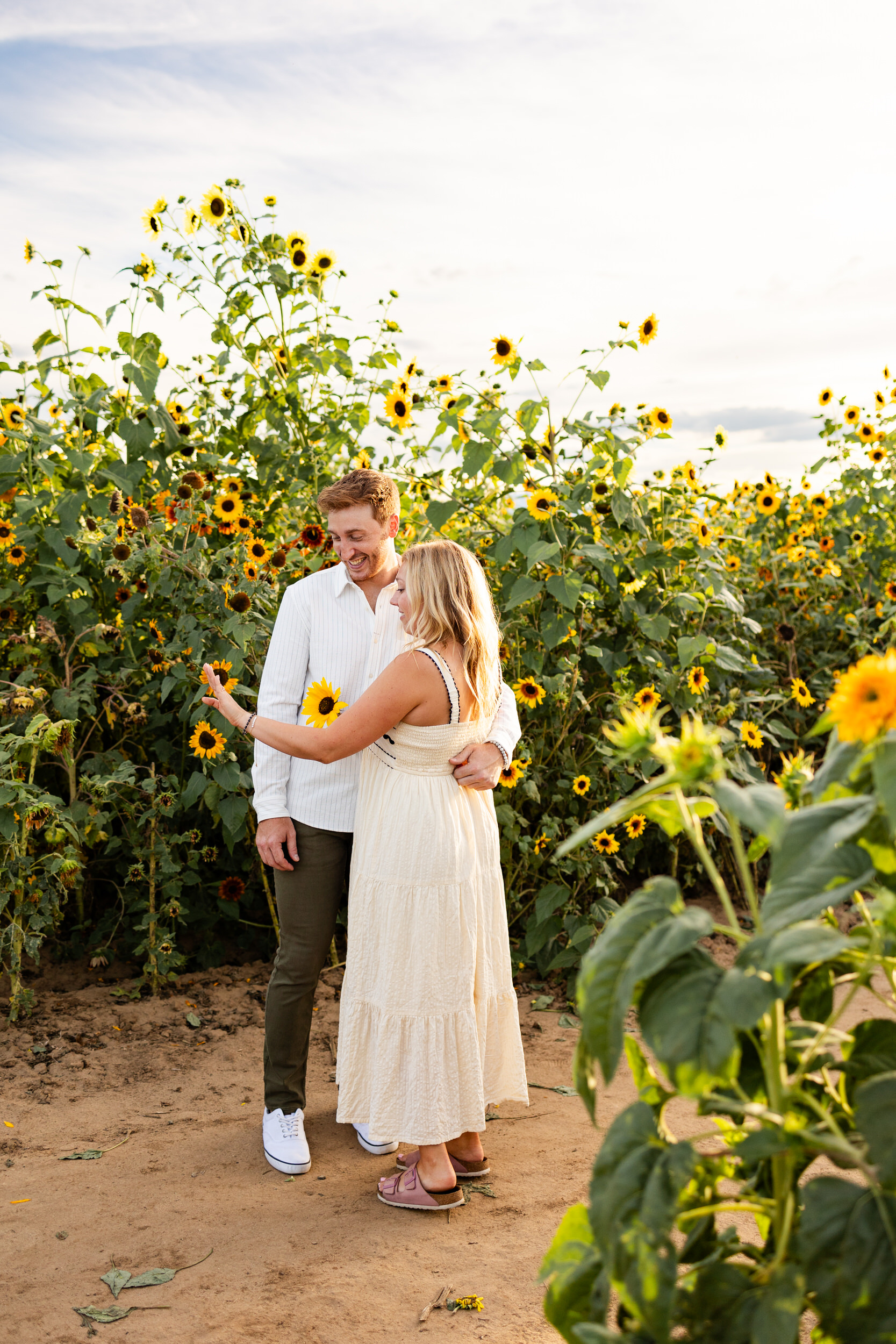 A newly engaged couple admires the engagement ring while standing in a sunflower field.