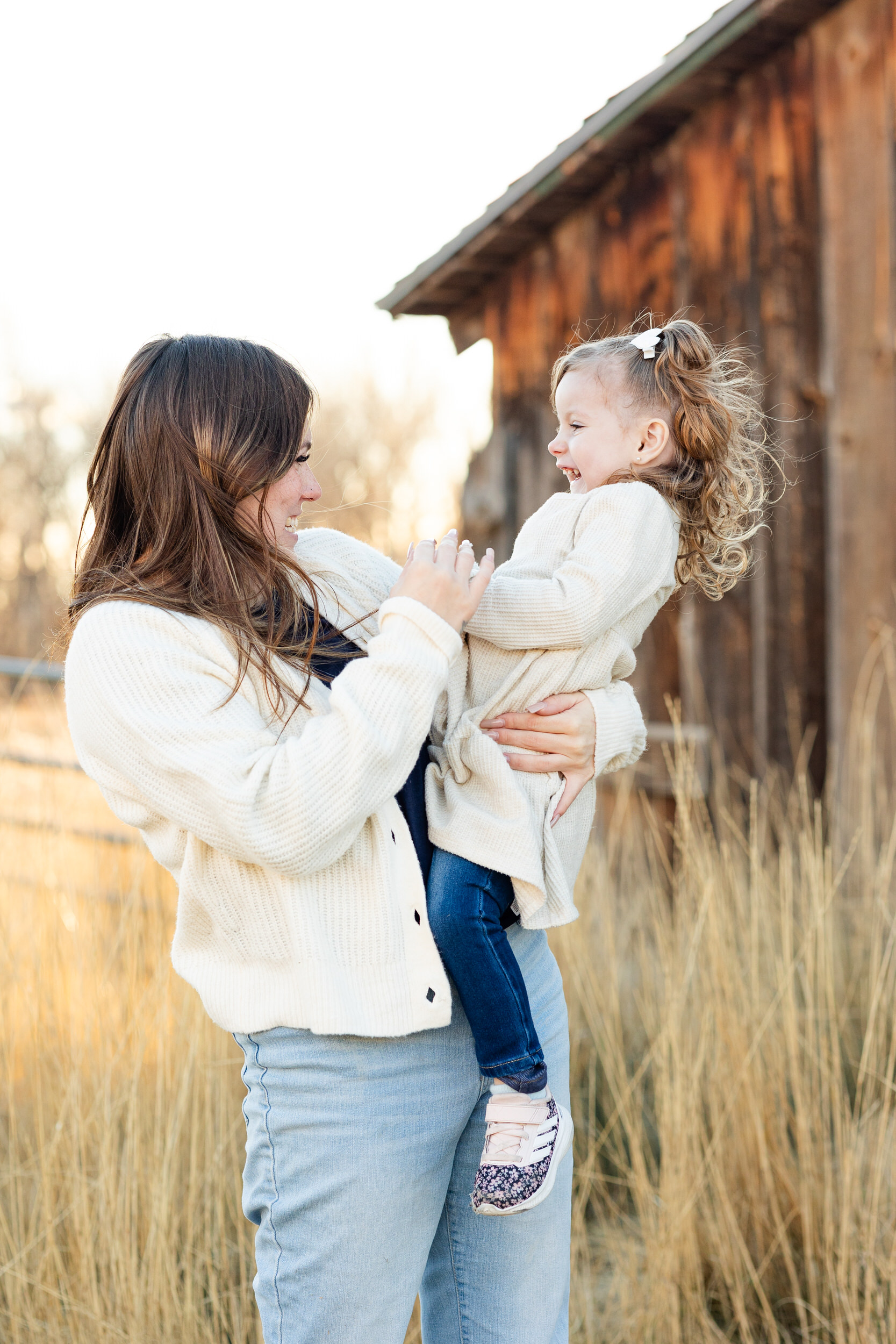 A mom holds her young daughter on her hip and they laugh with each other.