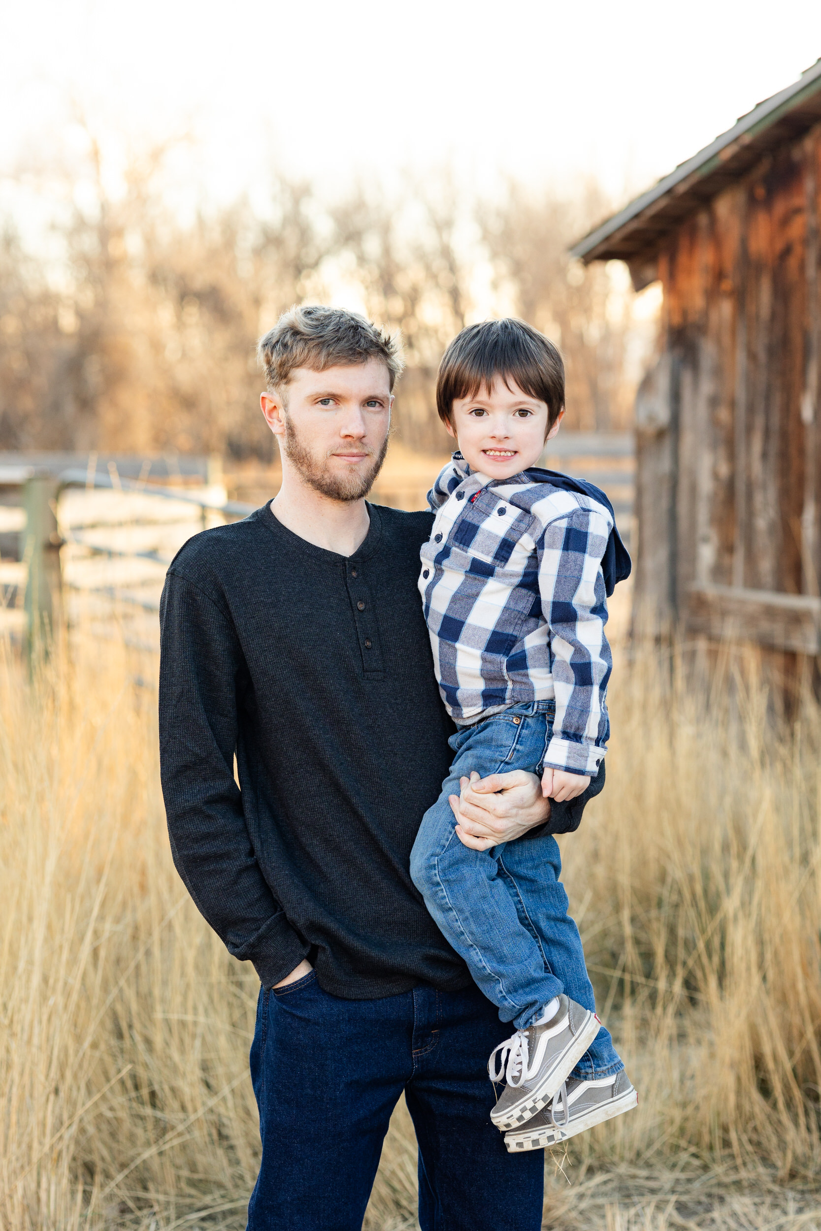 A dad holds his young son and they both look at the camera.