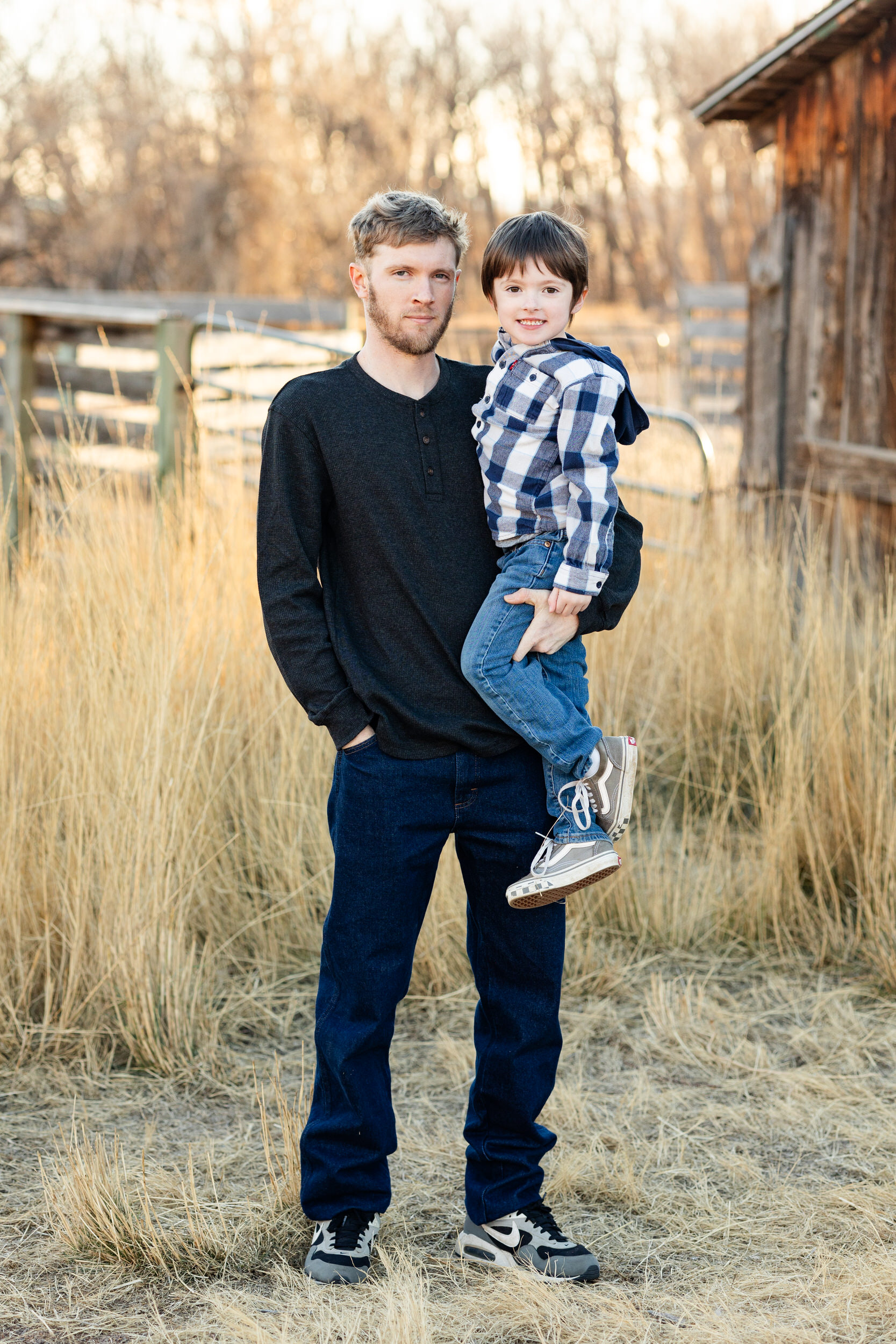 A dad holds his young son and they both look at the camera.