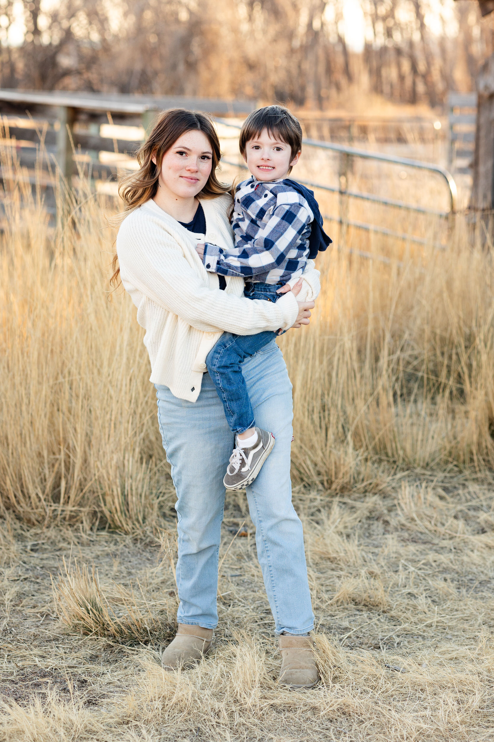 A mom holds her young son and they both smile at the camera.