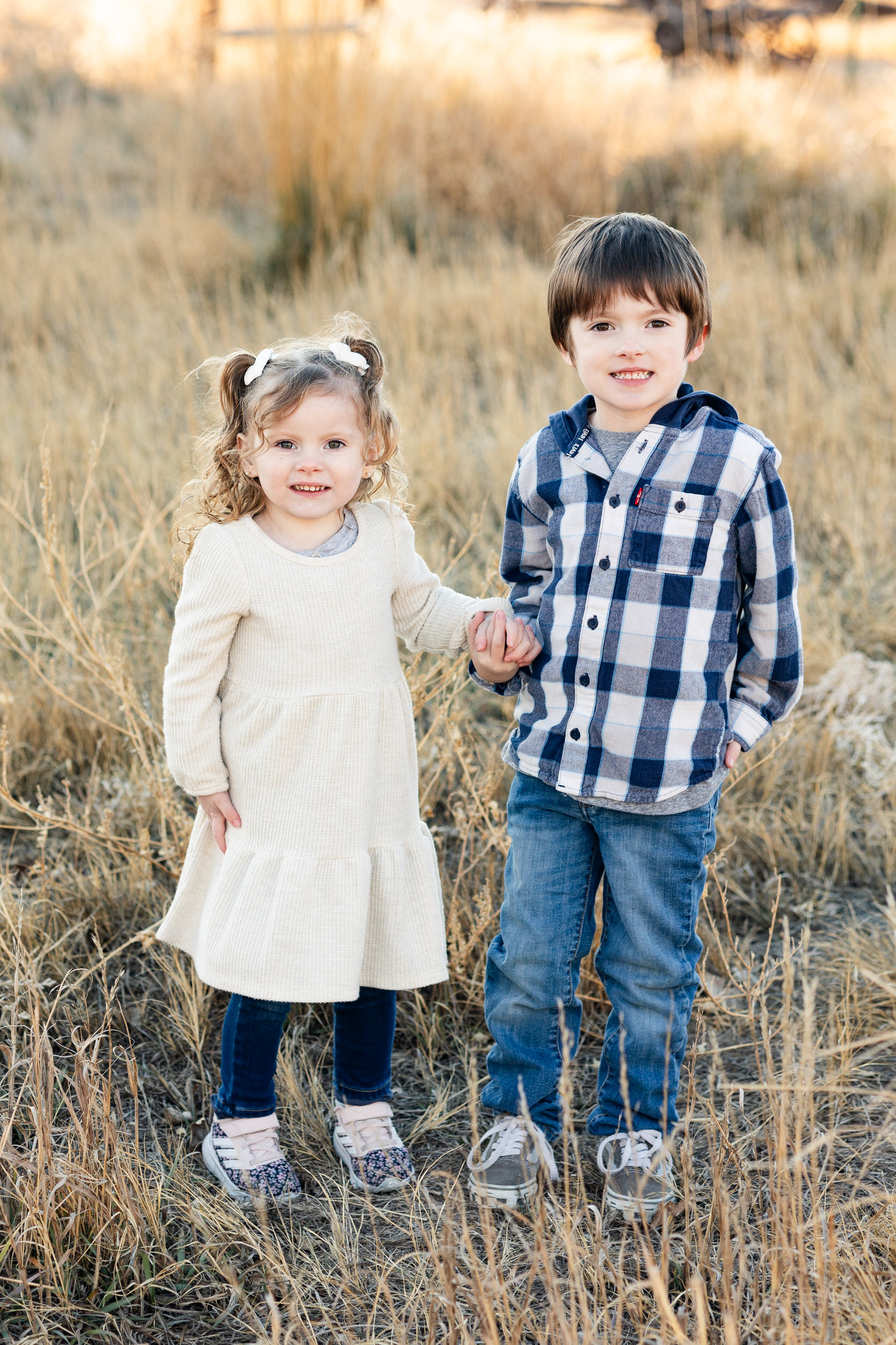 Young brother and sister hold hands and smile at the camera.