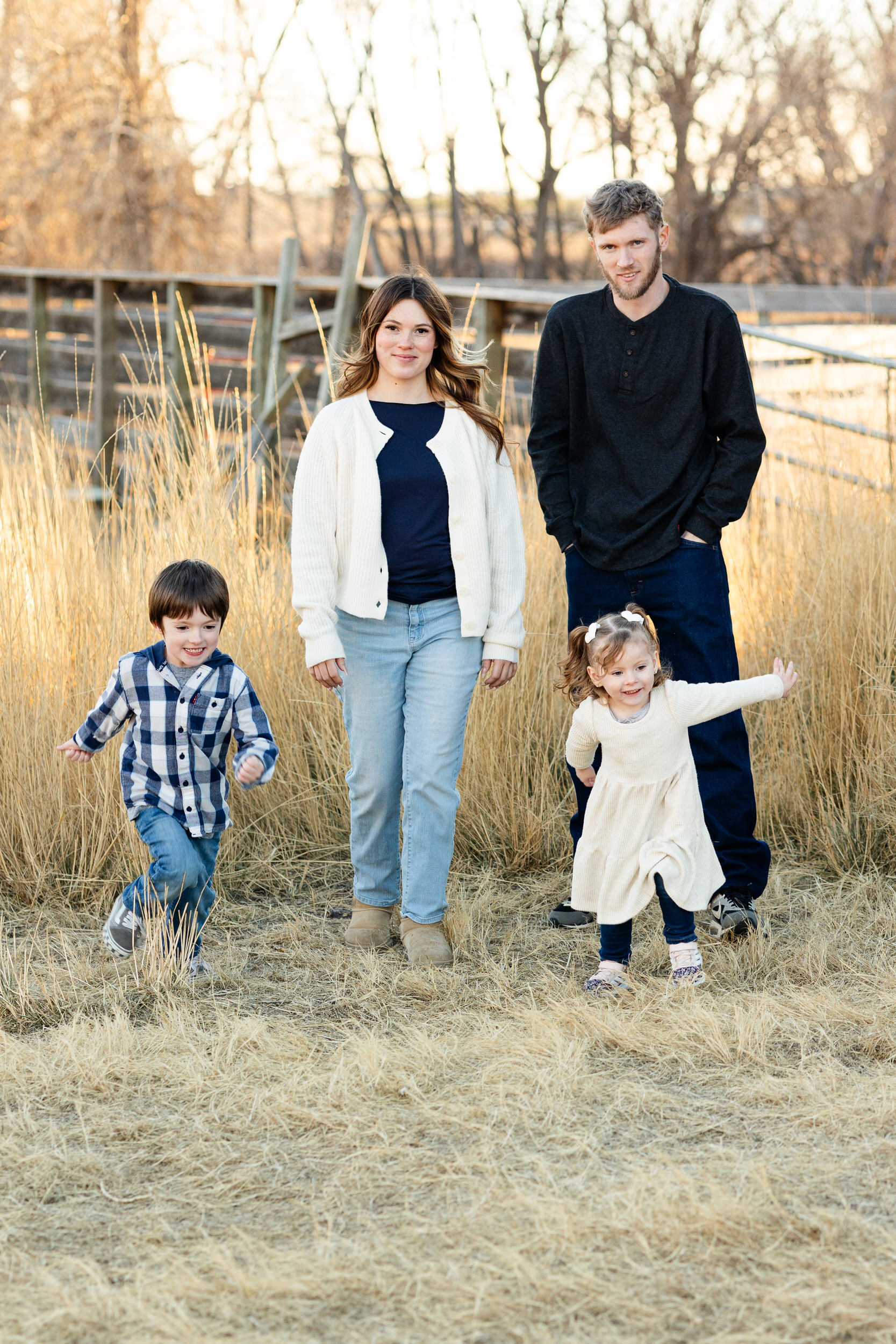 A young boy and girl run through a field ahead of their mom and dad.