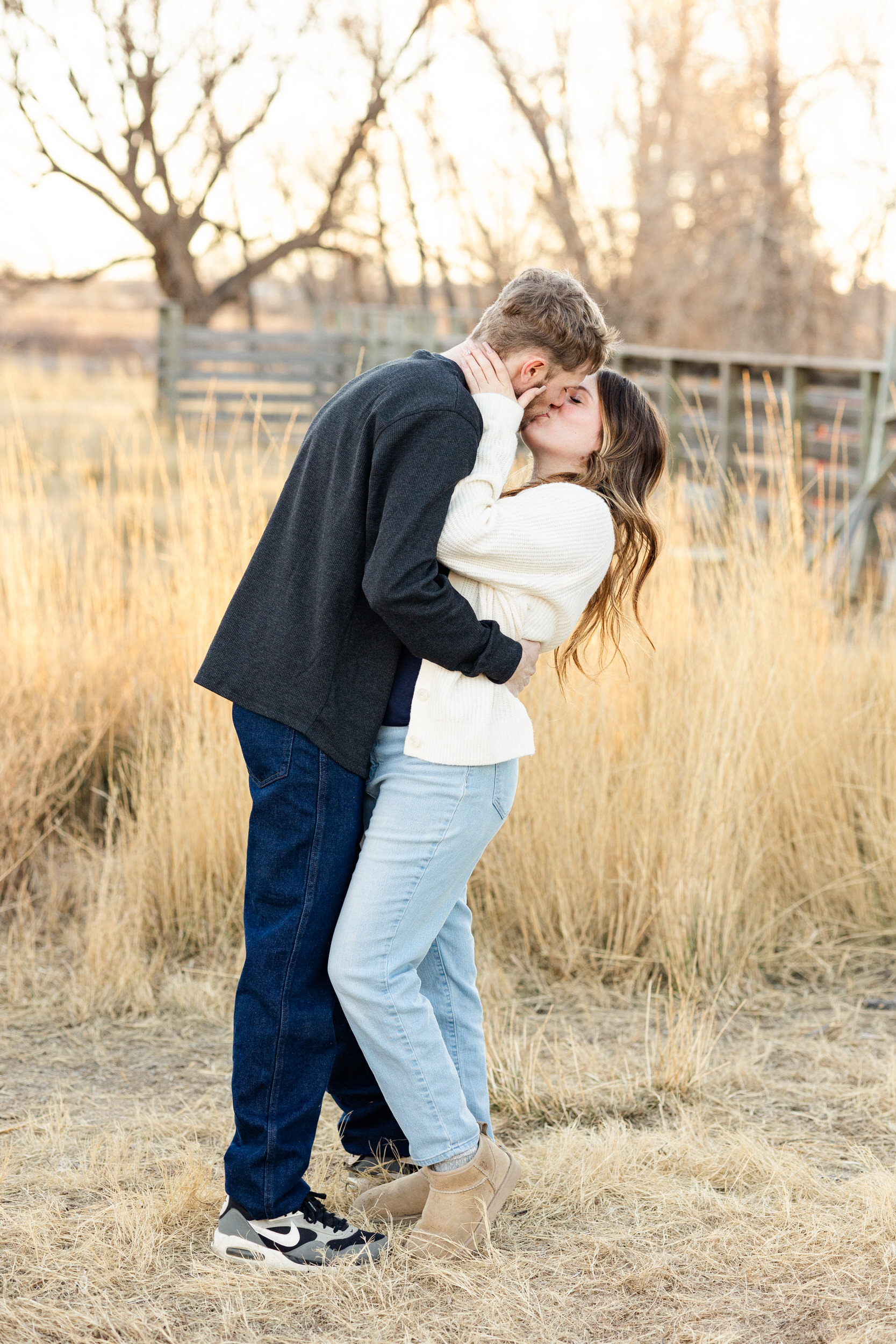 A couple shares a kiss in a field.