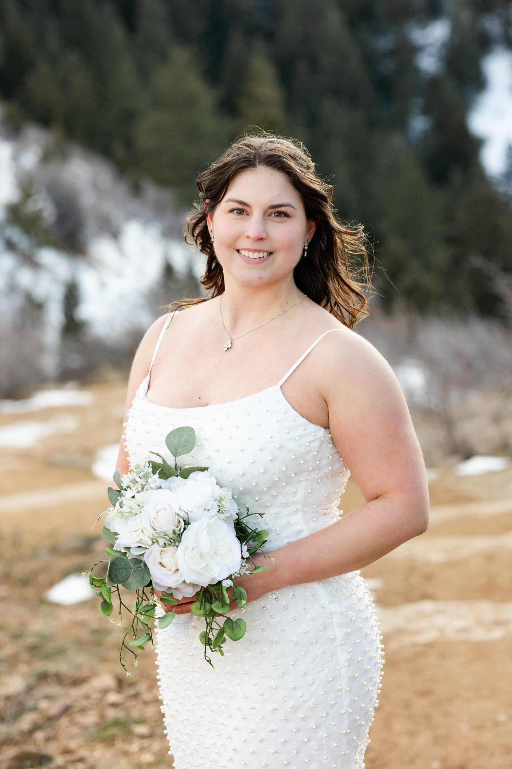 A woman in a white dress holds a bouquet of flowers and smiles at the camera.