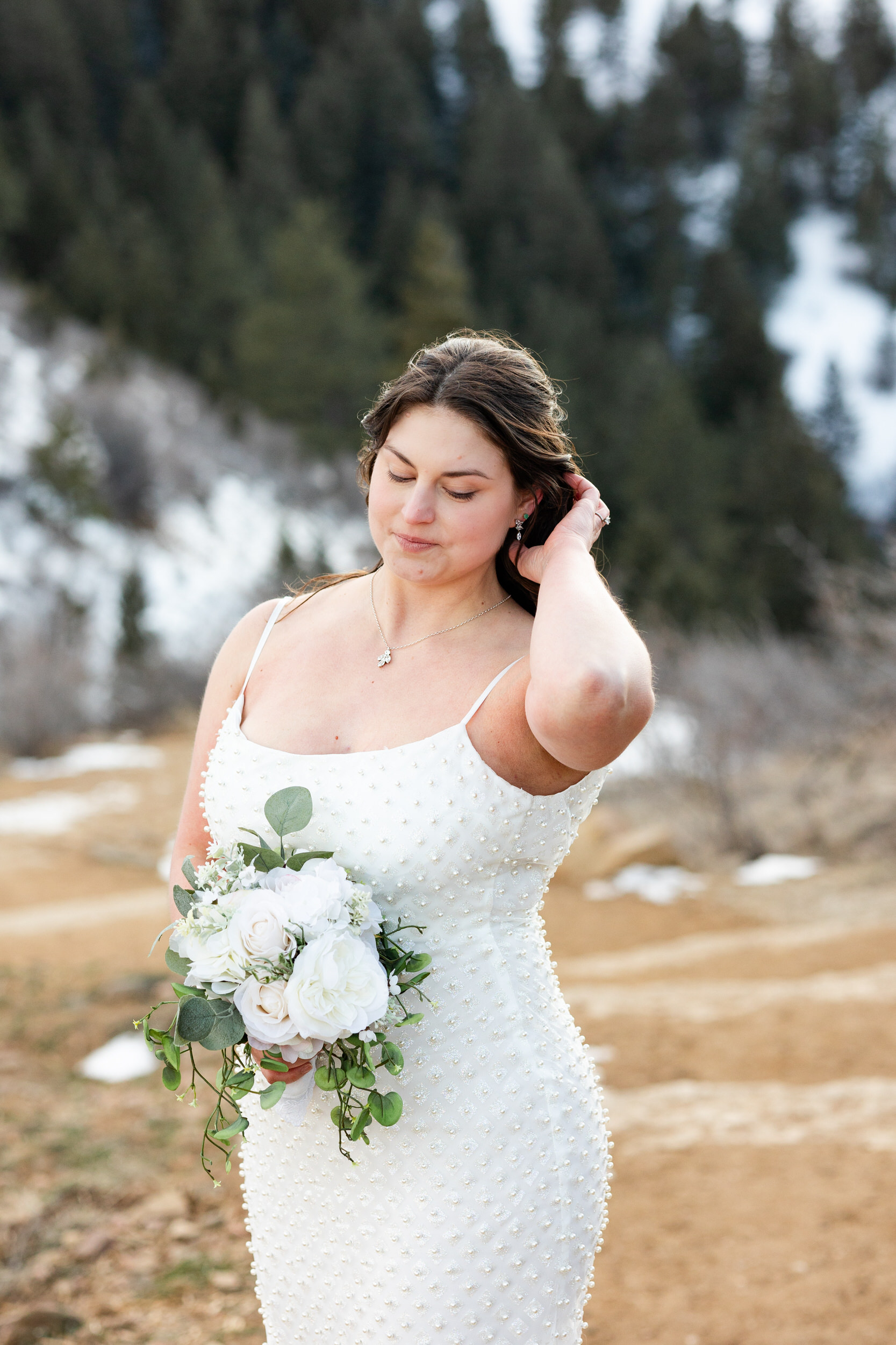 A woman in a white dress holds a bouquet of flowers and runs one hand through her hair.