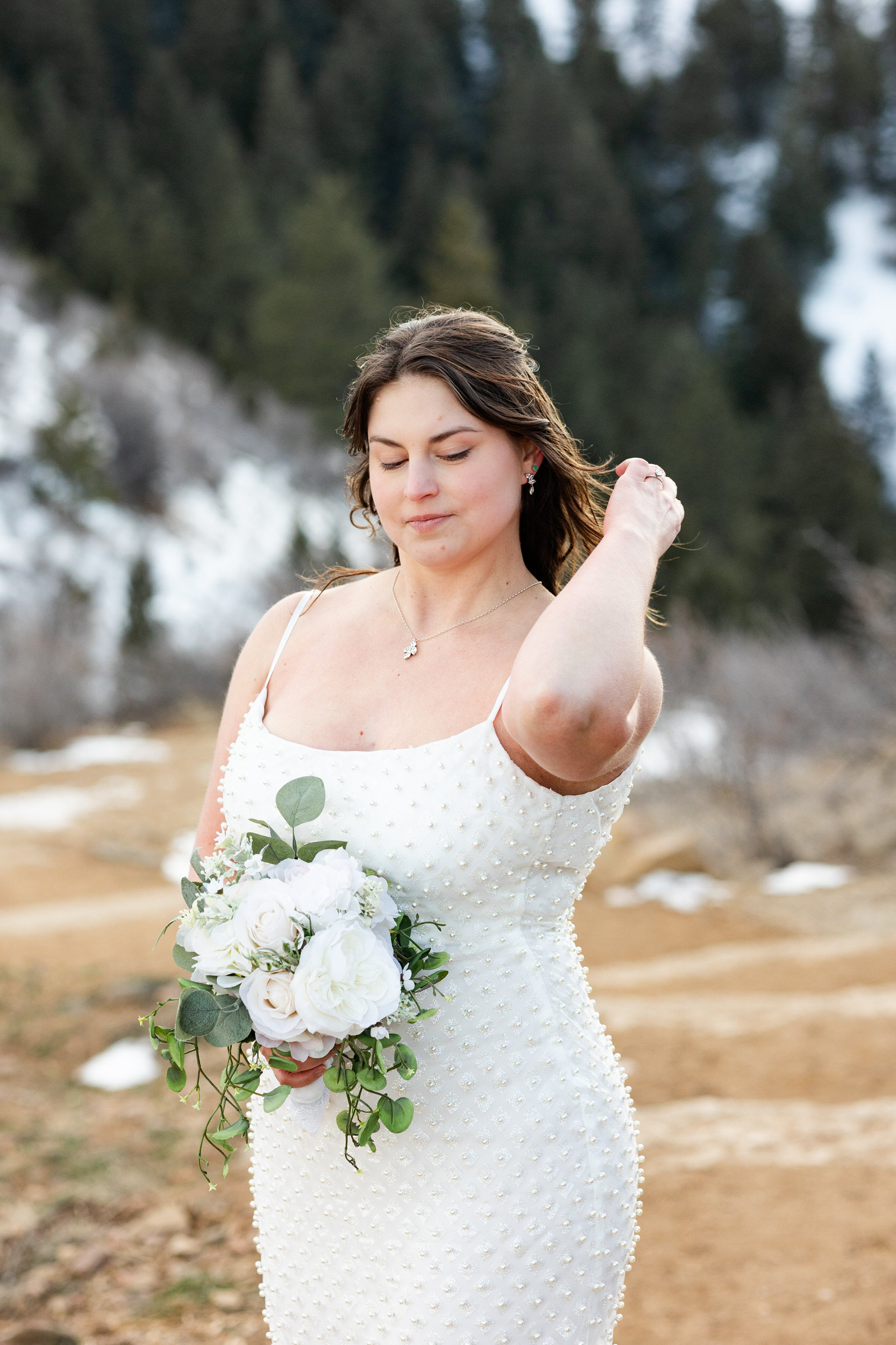 A woman in a white dress holds a bouquet of flowers and runs one hand through her hair.