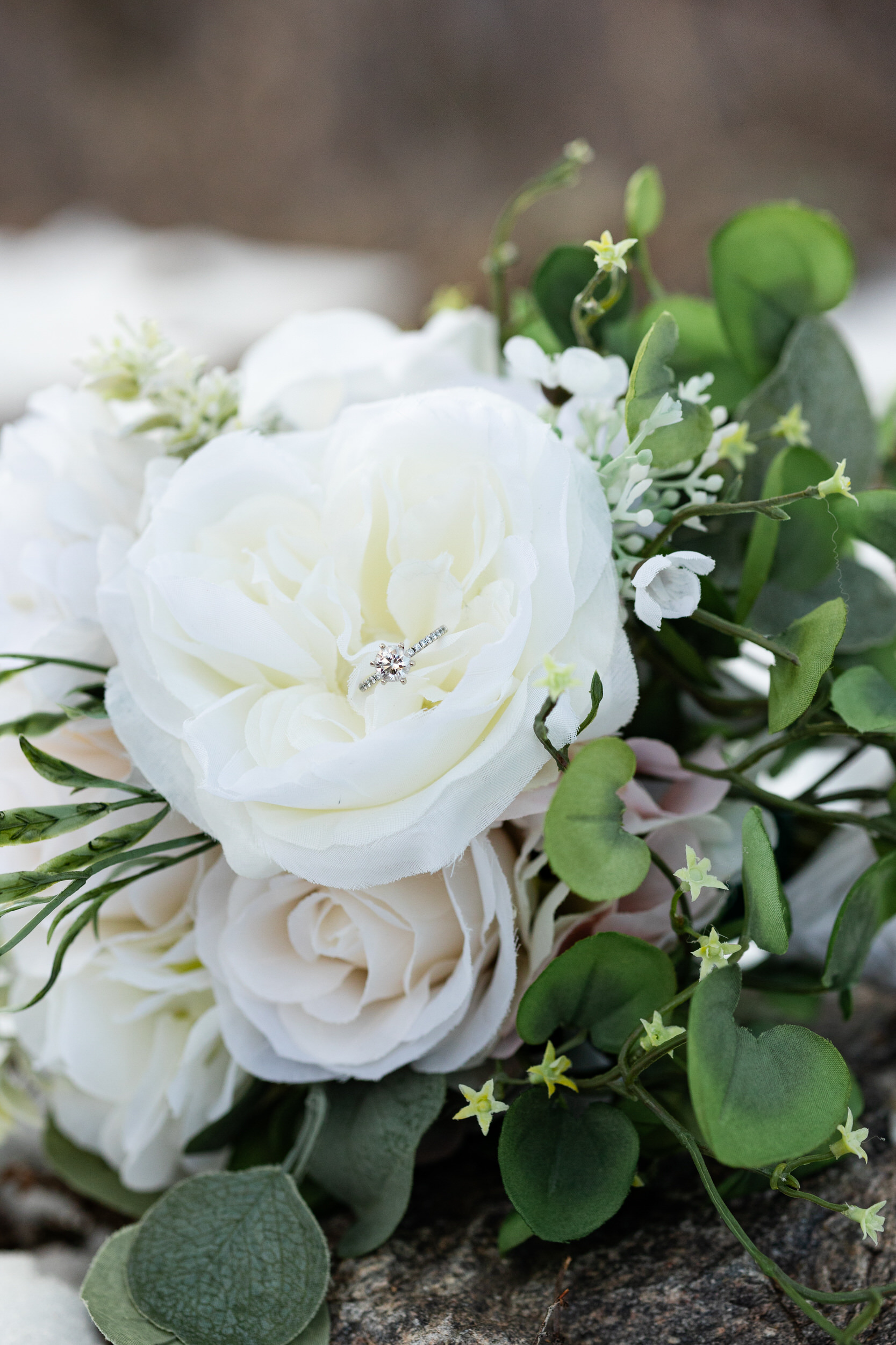 A wedding ring rests in a bouquet of white flowers.