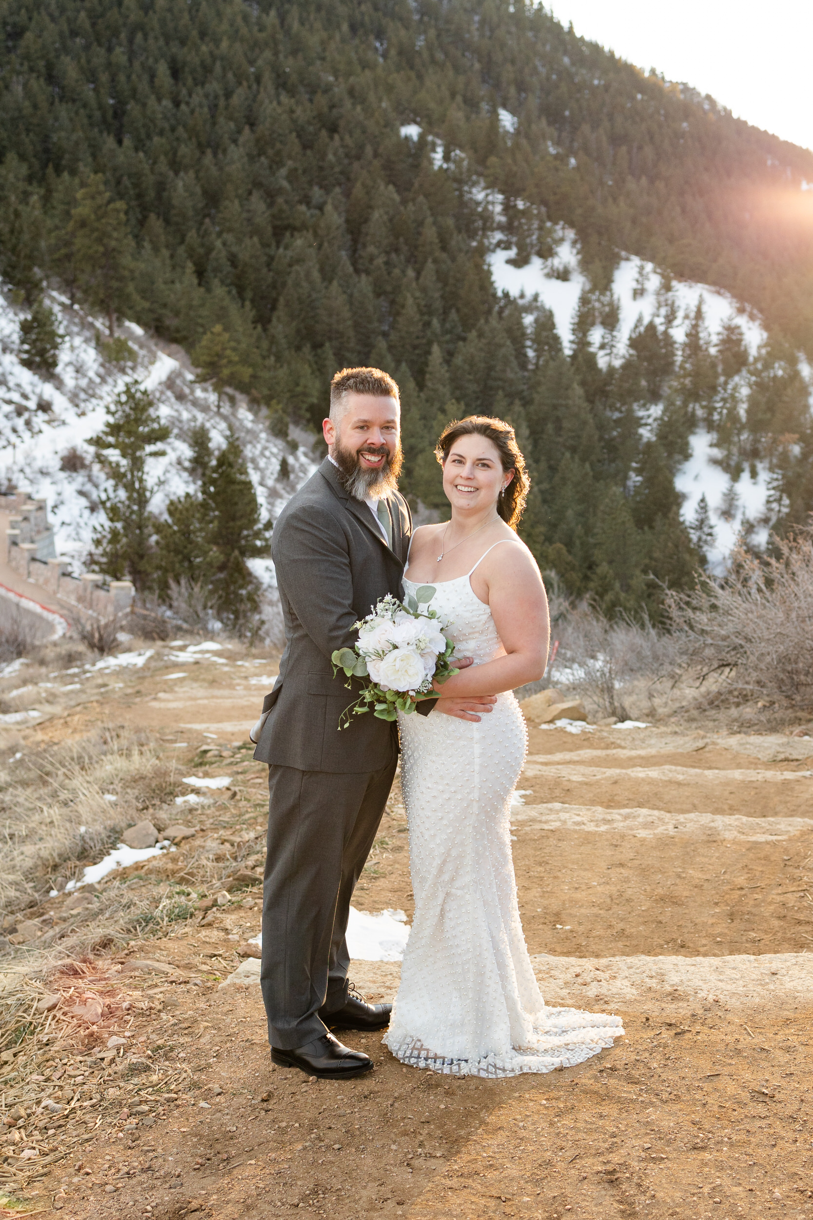 A husband and wife smile at the camera in the mountains.