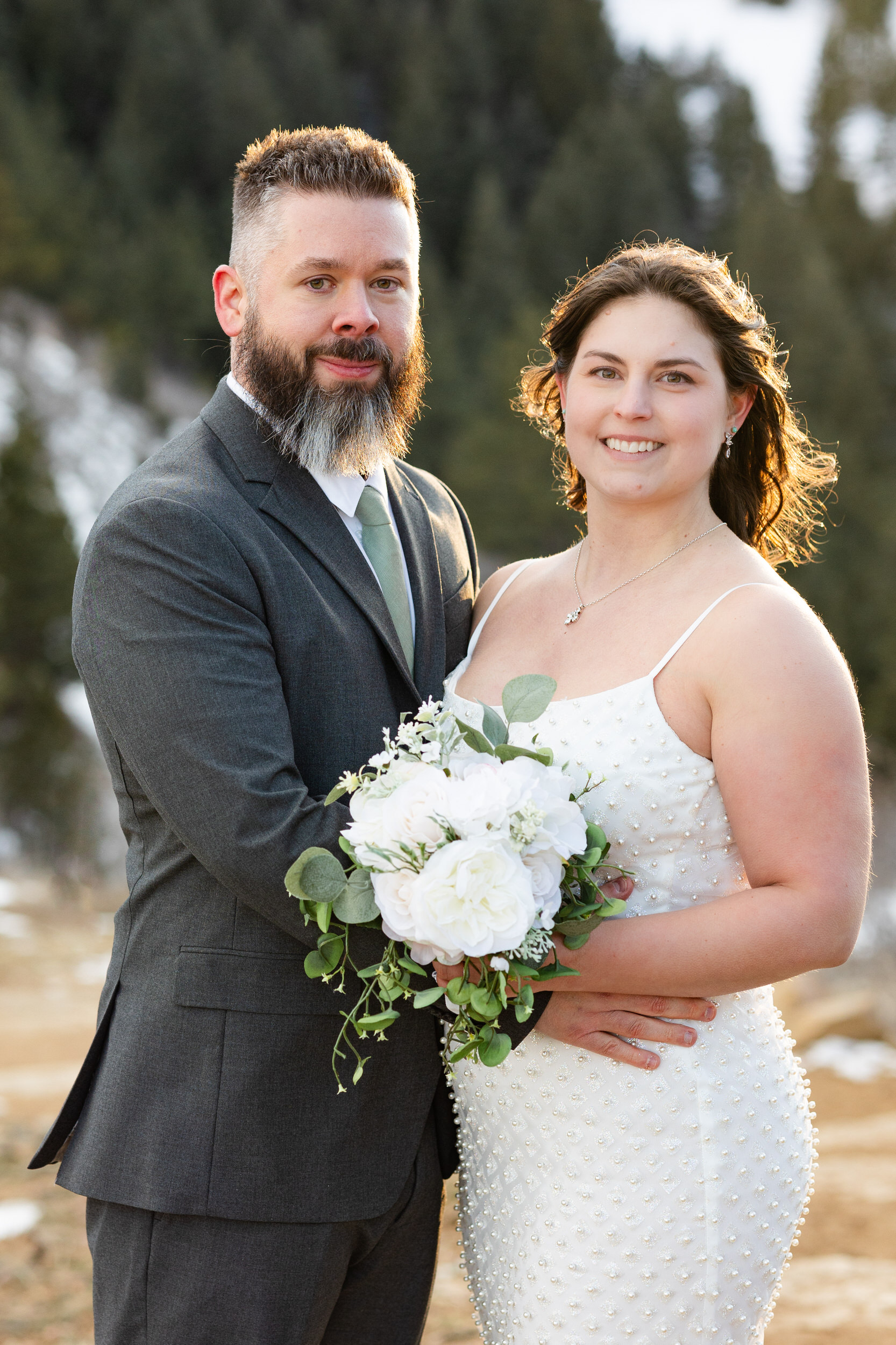 A husband and wife in wedding attire smile at the camera.