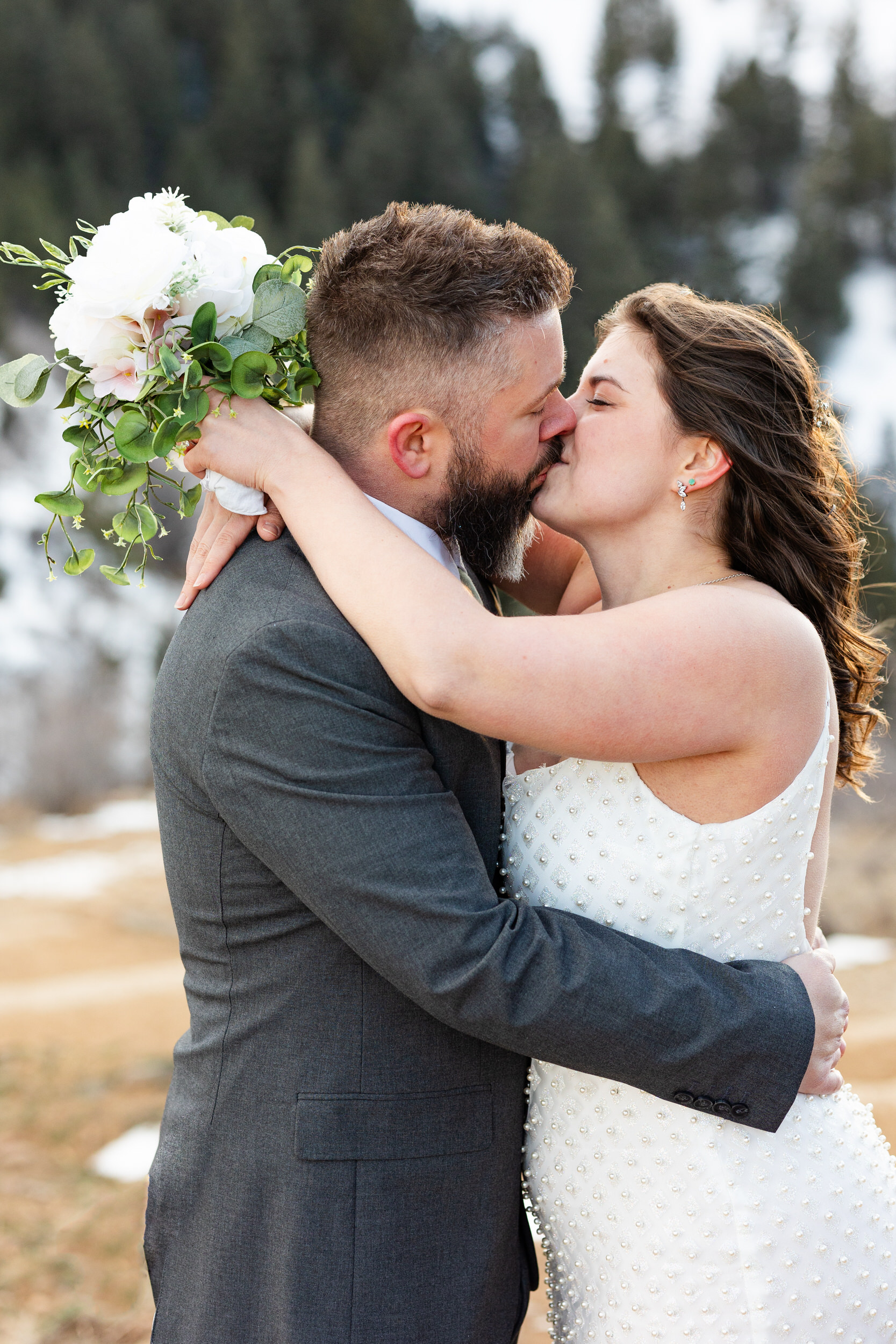 A husband and wife in wedding attire share a kiss.