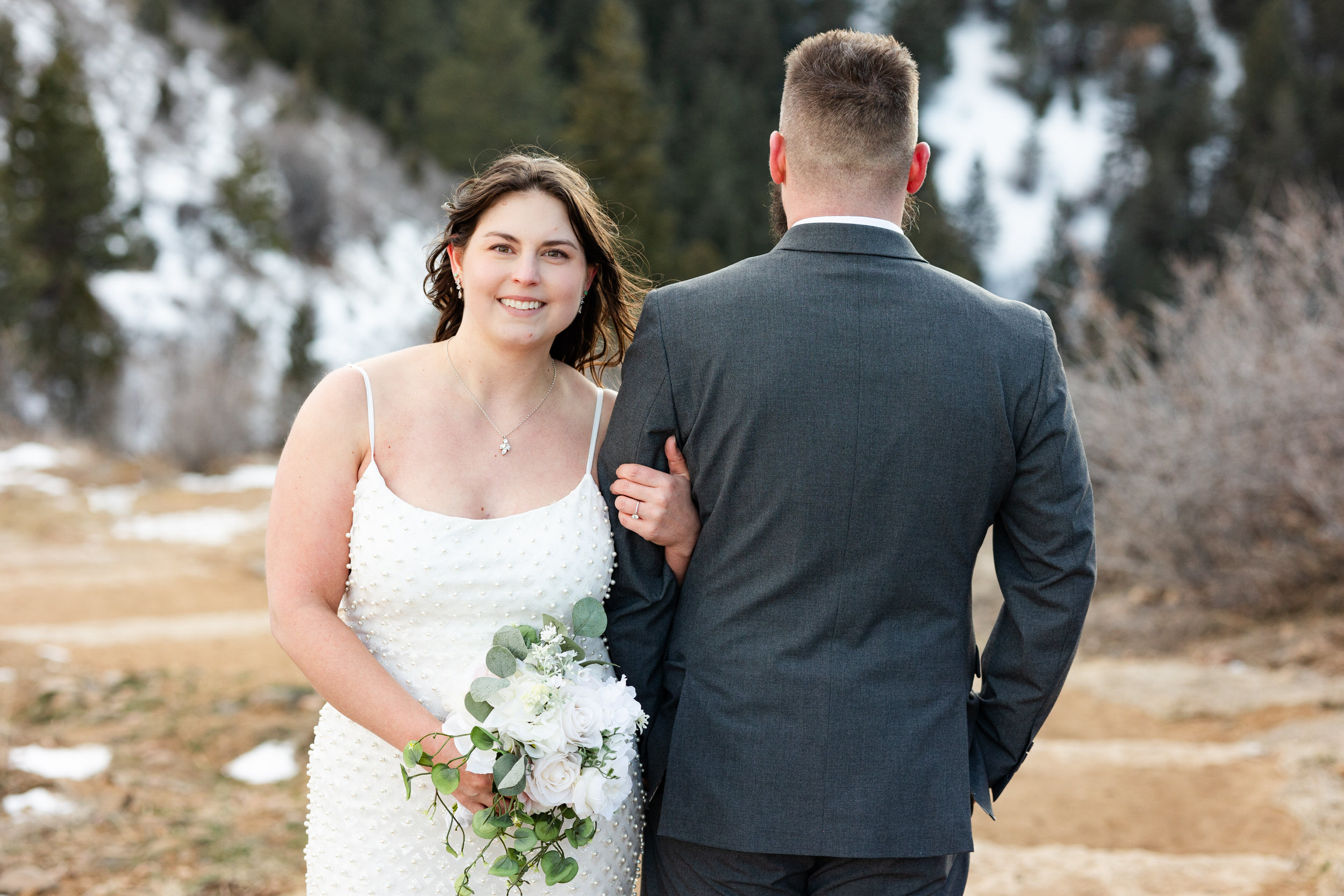 A man turns his back to the camera and his wife loops her arm through his as she faces the camera and smiles.
