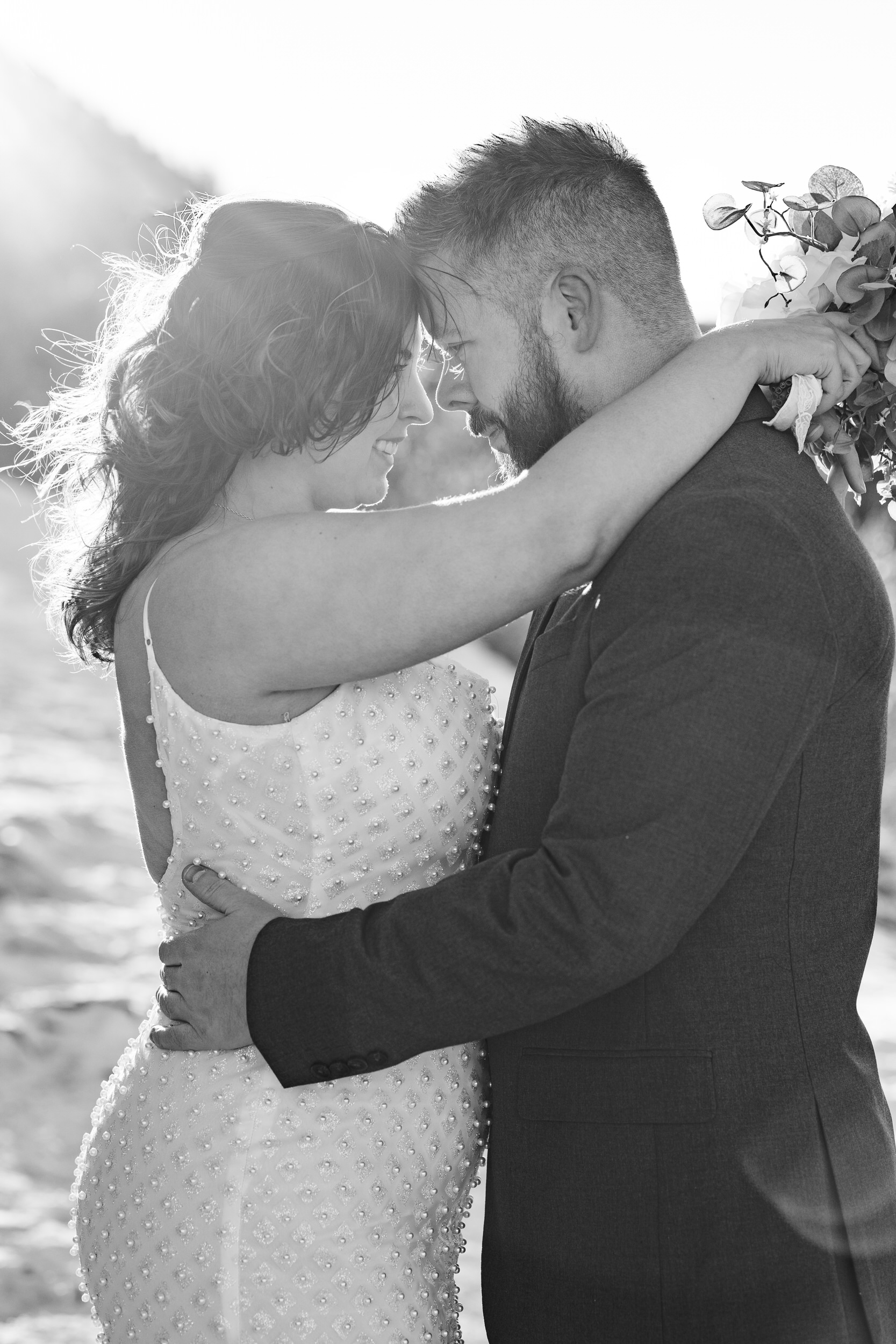 A husband and wife stand forehead to forehead and smile at each other.
