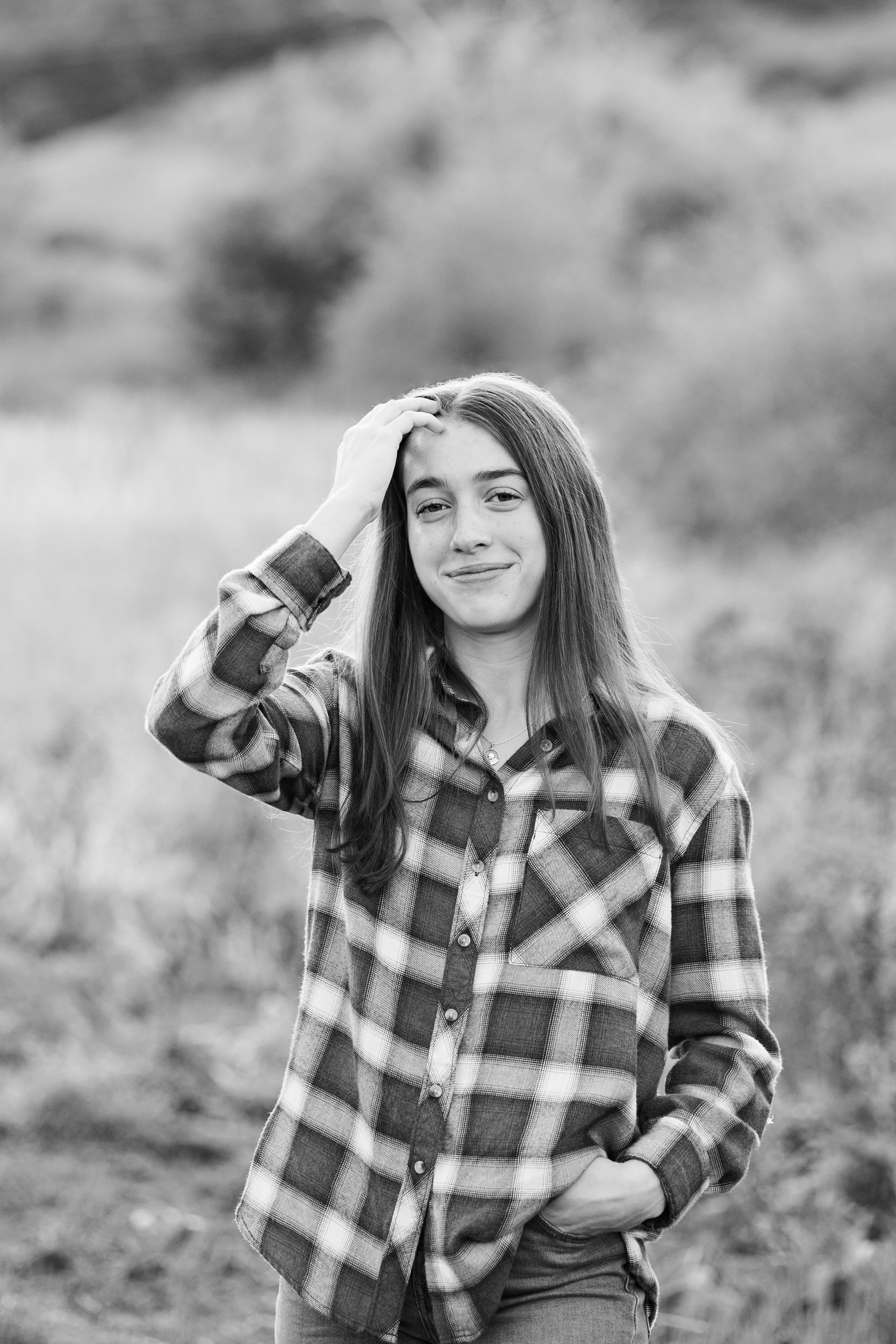 A young woman in a flannel shirt runs her hand through her hair and smiles at the camera.